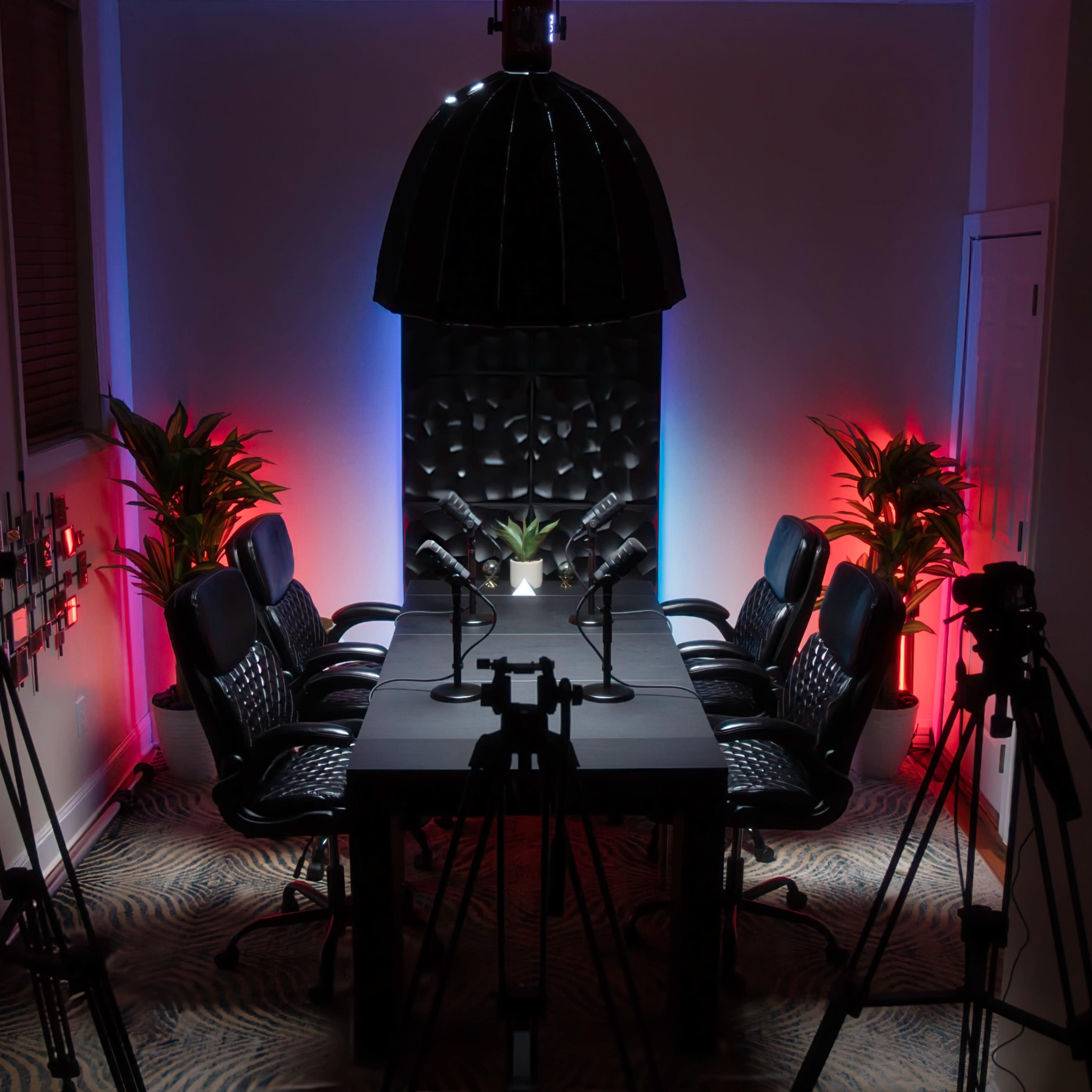 A modern conference room is set up with a long table, eight black chairs, and microphones, surrounded by potted plants and illuminated with colored lights.