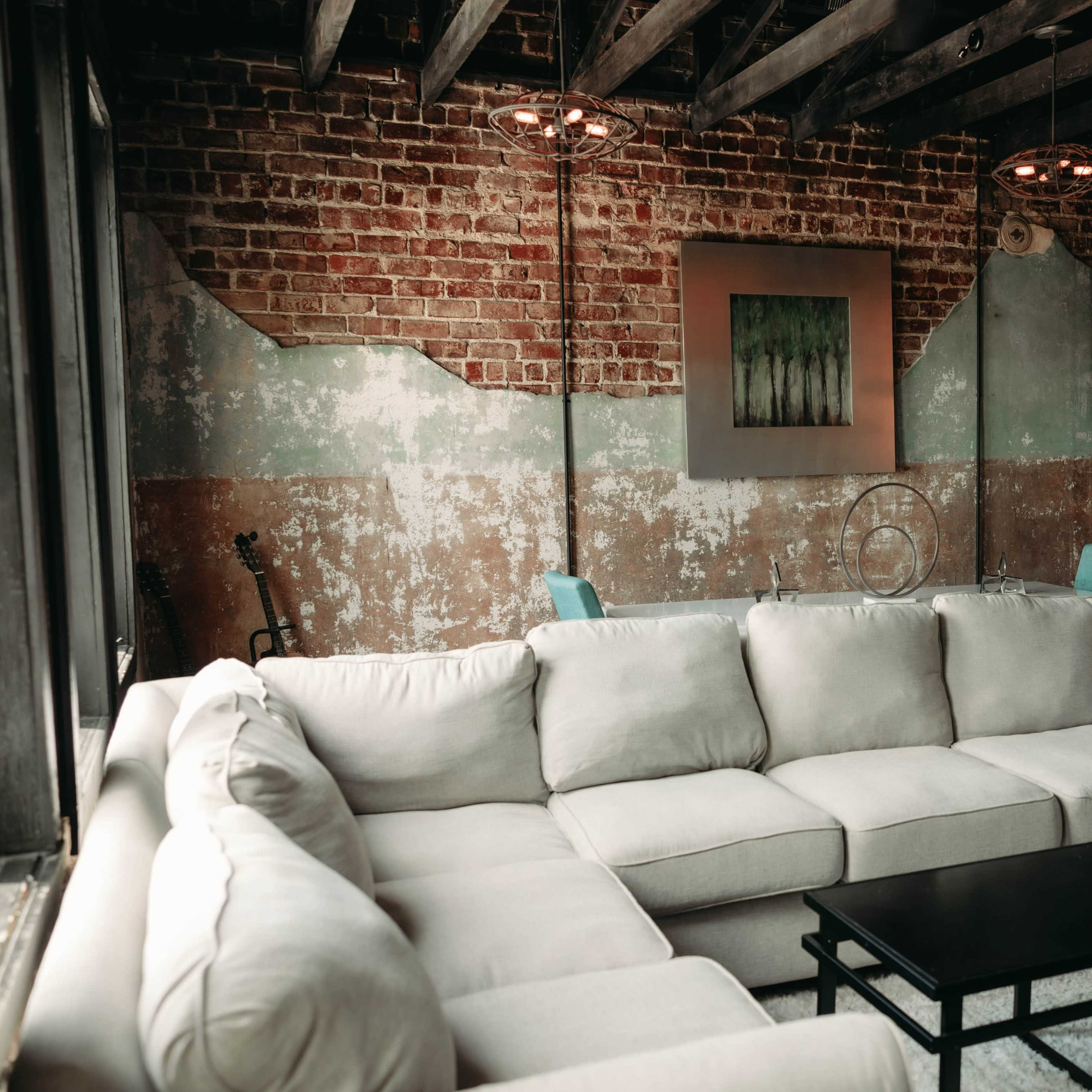 A modern living room with a large beige sectional sofa, a black coffee table, and exposed brick walls featuring a mix of textures and colors.