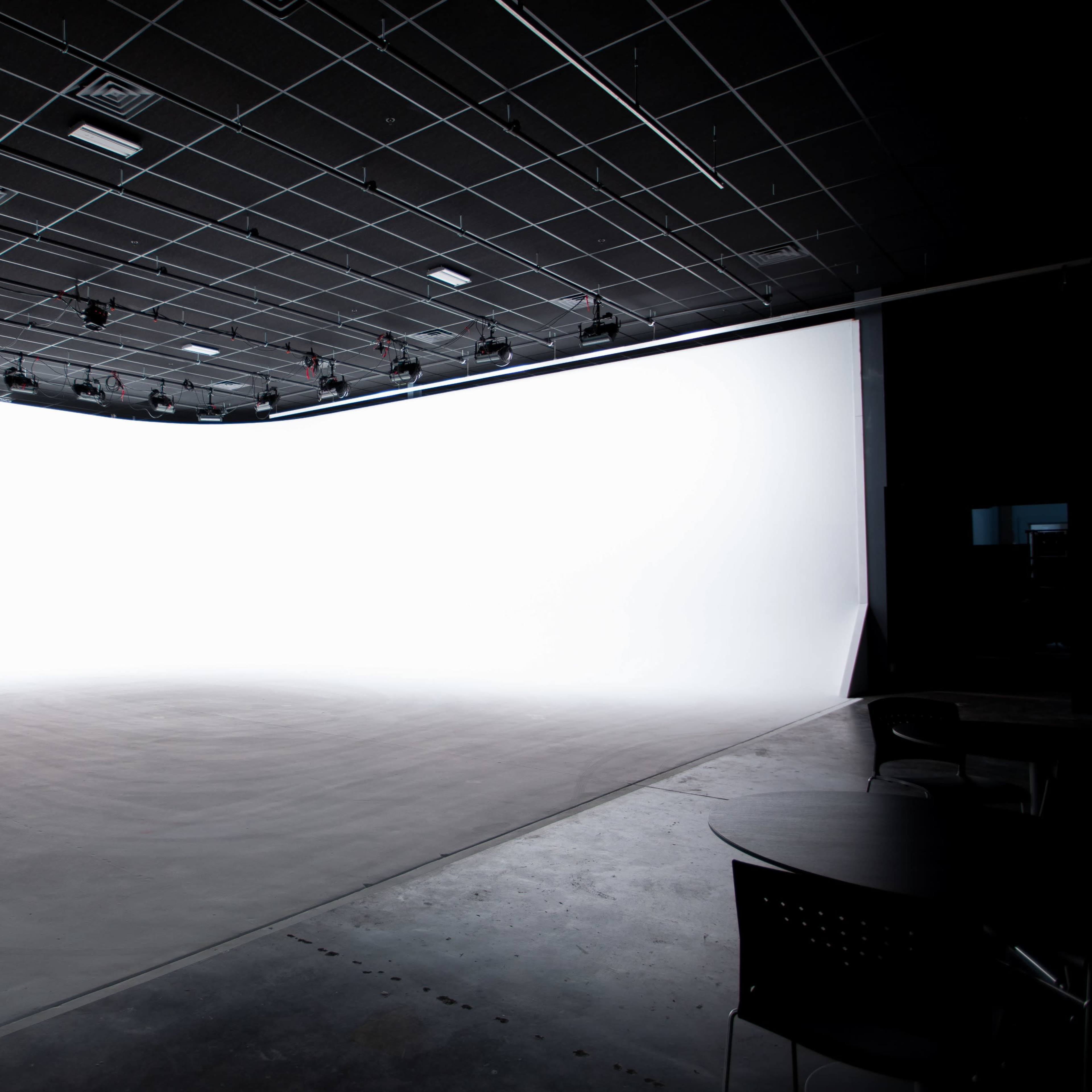 A spacious studio features a large white backdrop with a smooth floor and overhead lighting.