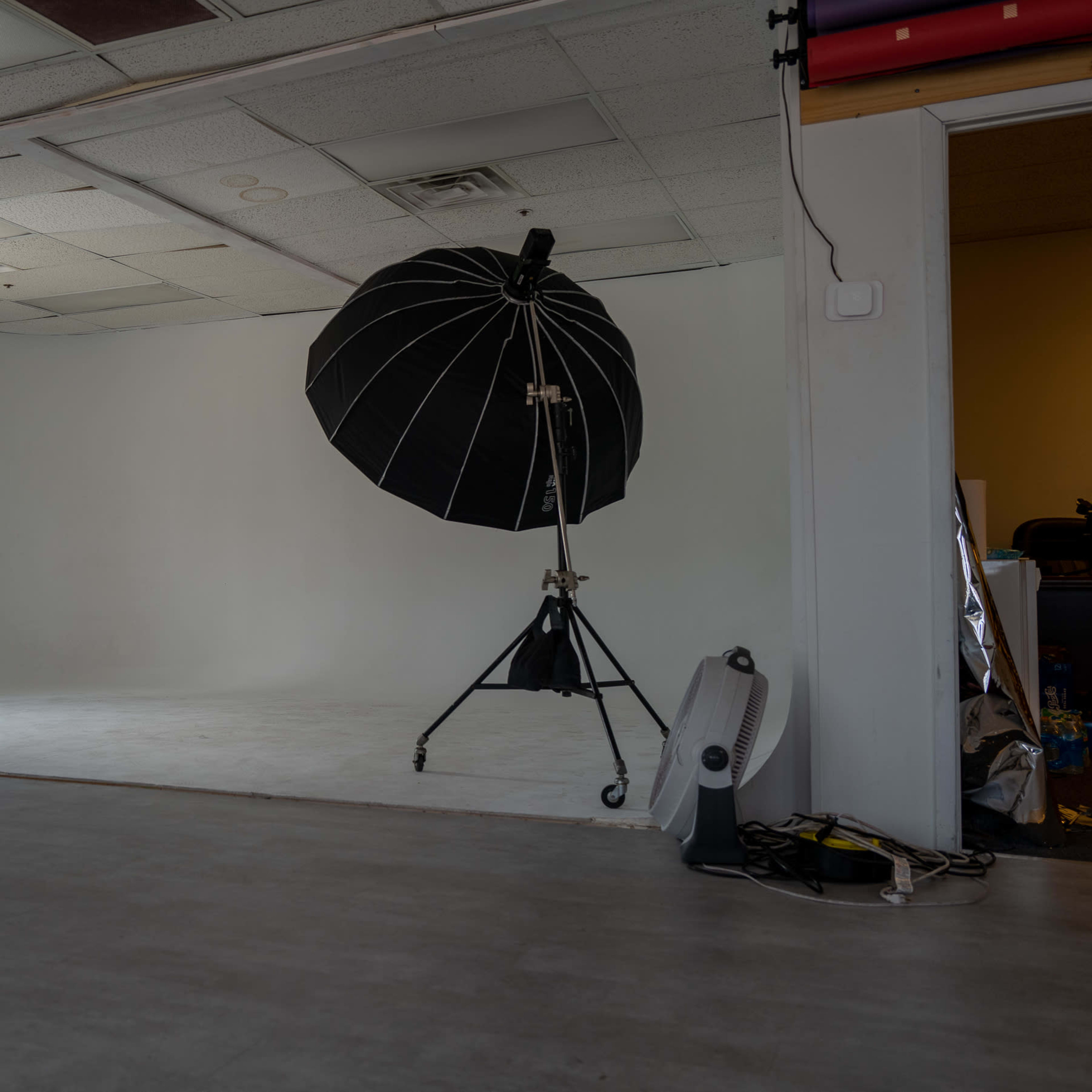 A spacious studio with a large black umbrella softbox on a stand, a white backdrop, and minimal furnishings.