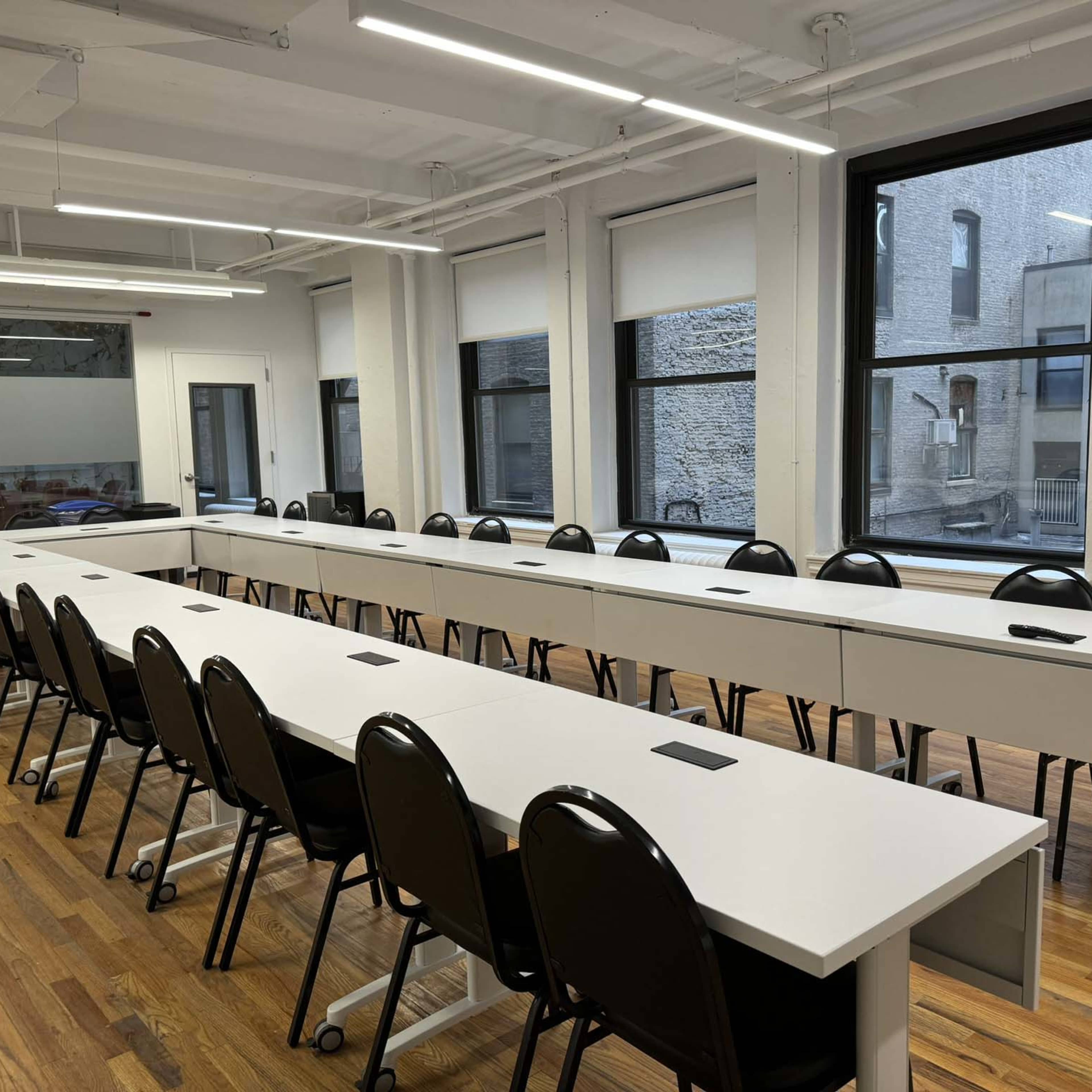 A spacious conference room with a long, white table surrounded by black chairs and large windows.