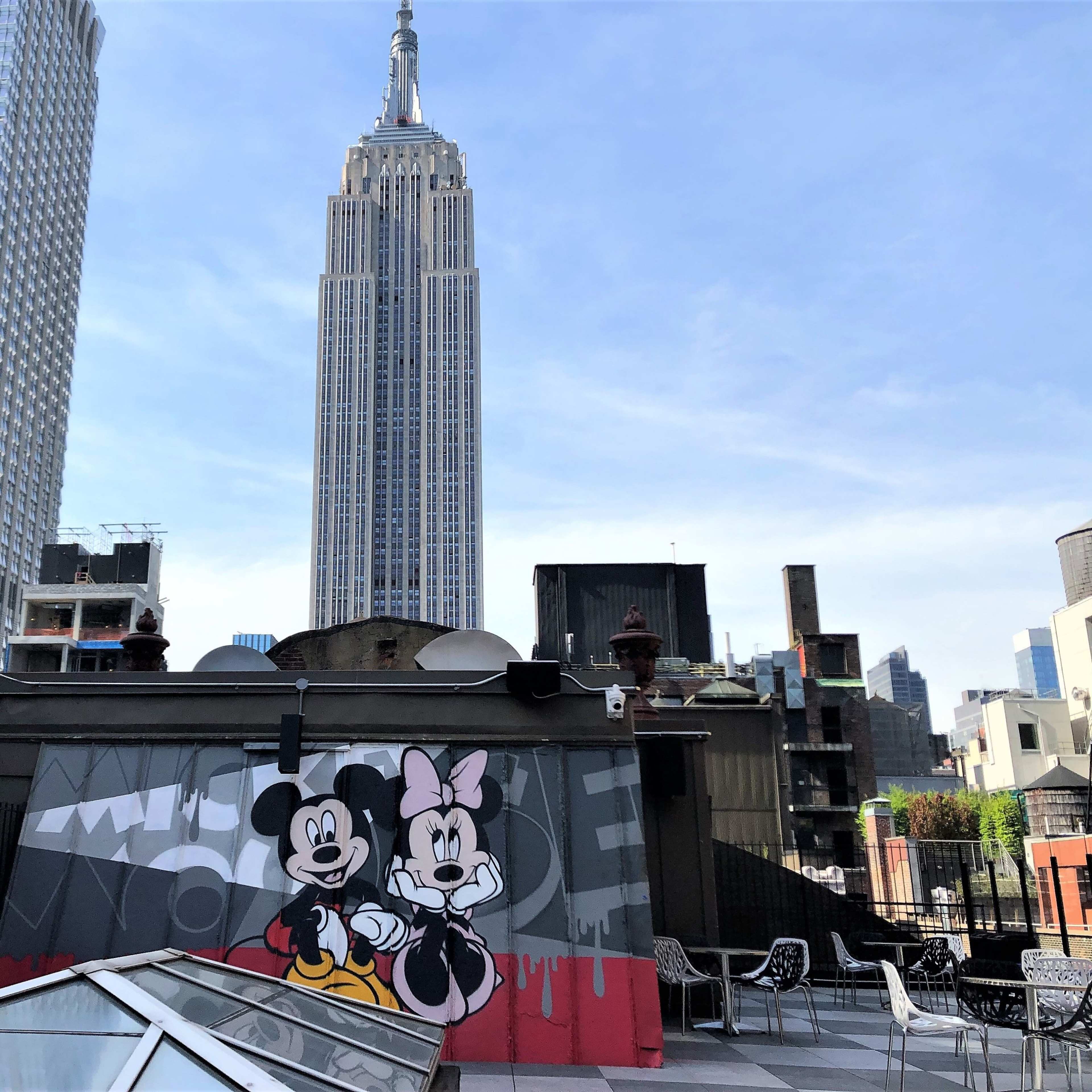 A rooftop view featuring a mural of Mickey and Minnie Mouse with the Empire State Building in the background.