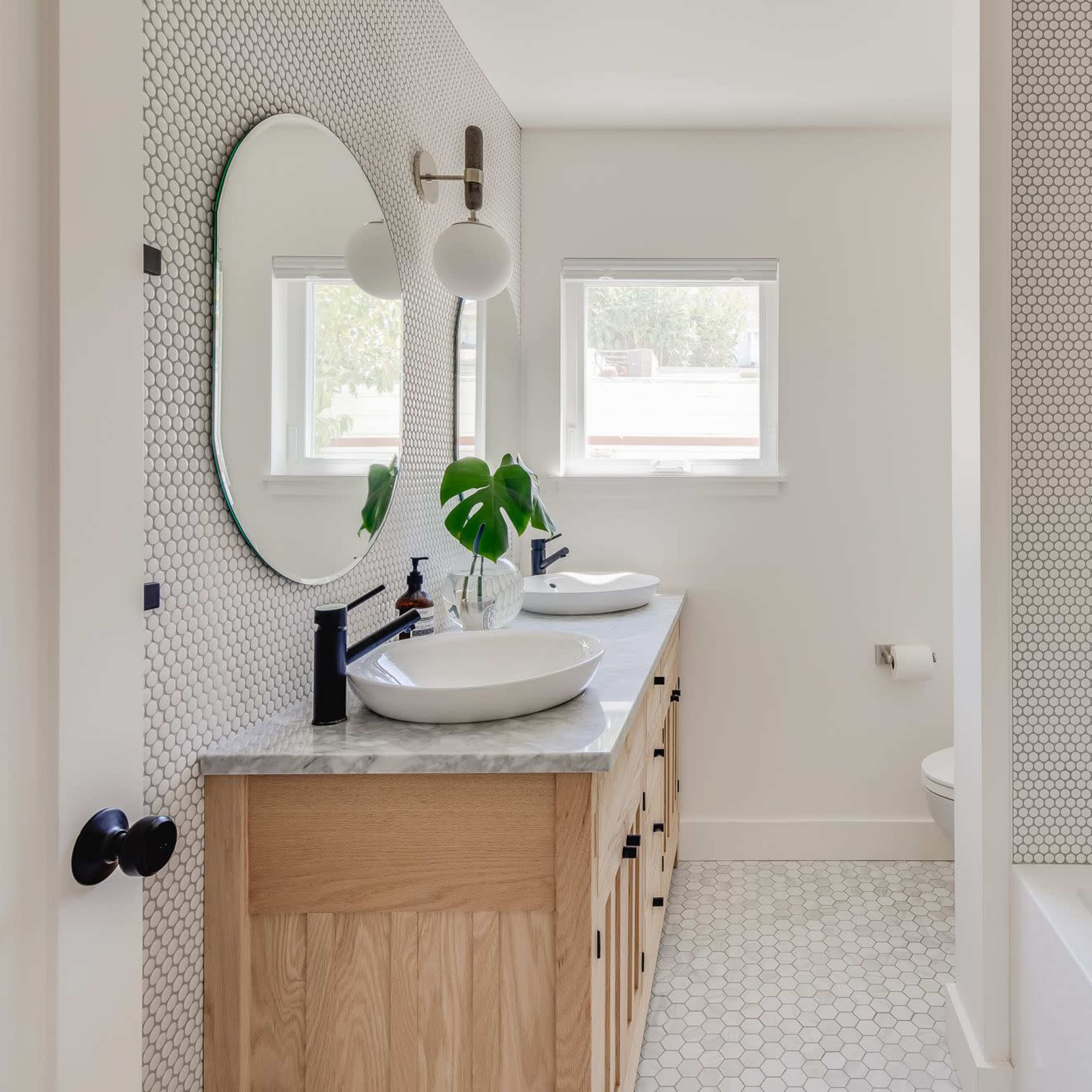 A modern bathroom featuring a double sink with circular mirrors, a shower area, and a bathtub, all designed with hexagonal tiles and neutral colors.