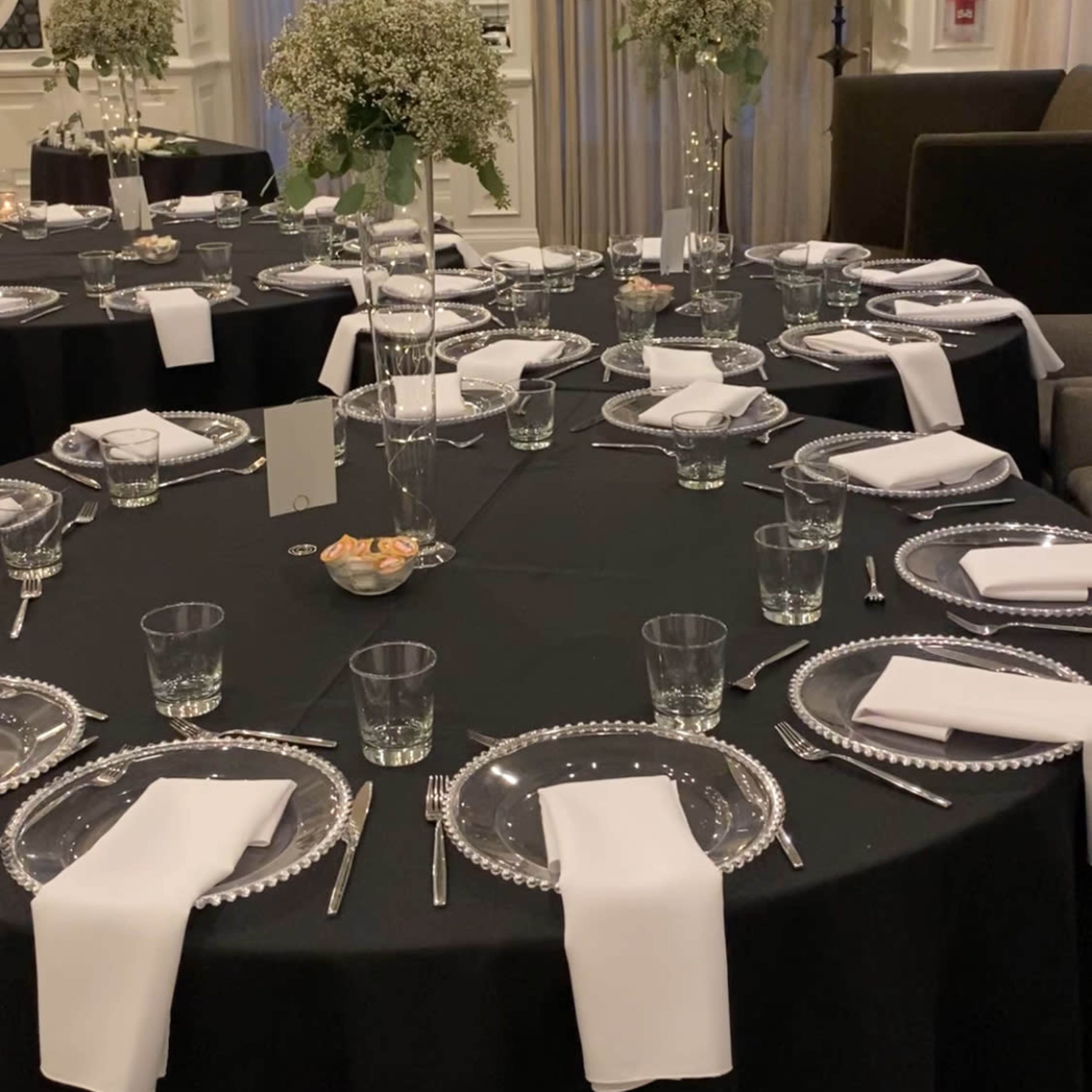 Elegantly set dining tables with black tablecloths, clear glassware, white napkins, and floral centerpieces.