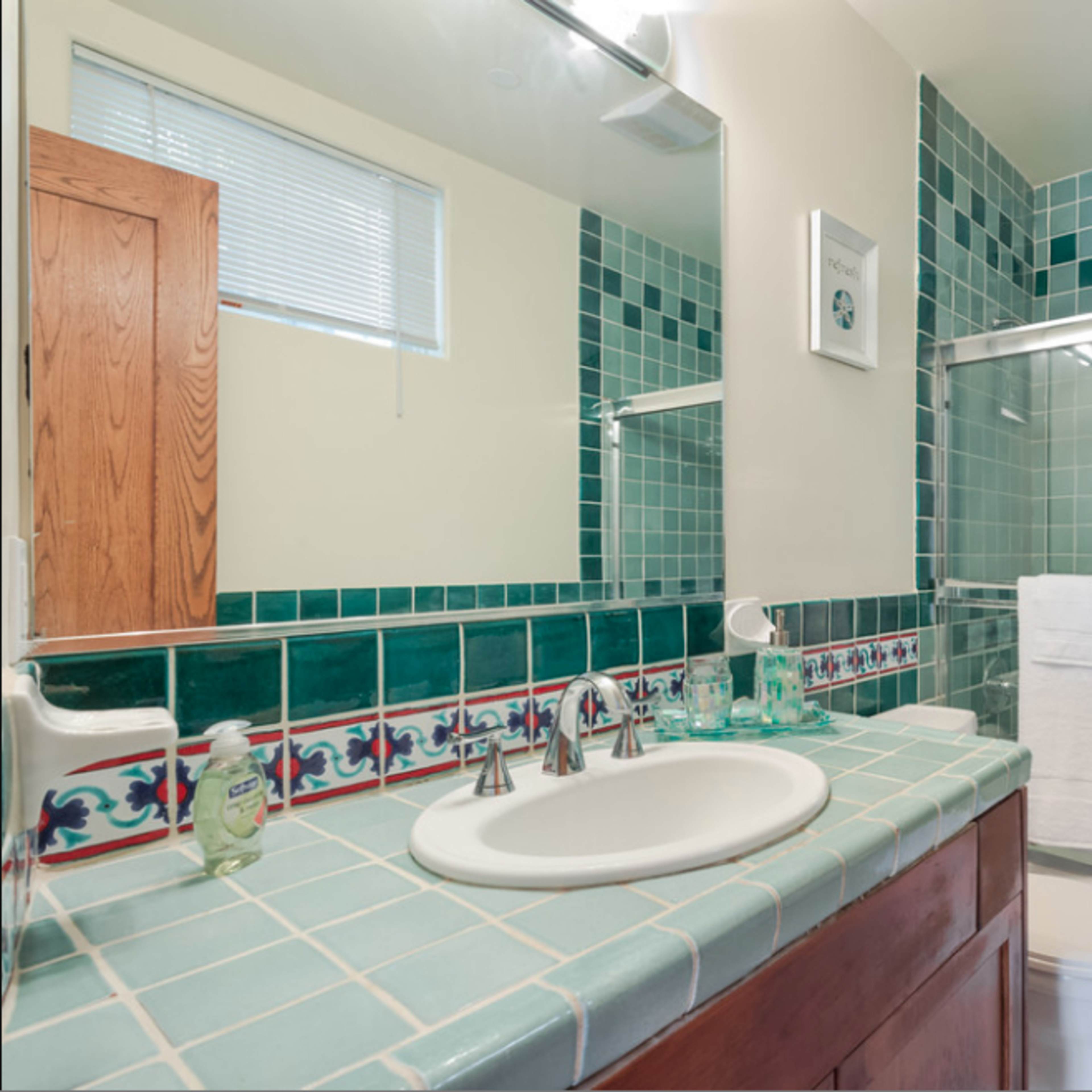 The bathroom features teal tiled walls, a white sink, a toilet, and a bathtub with a glass shower door.