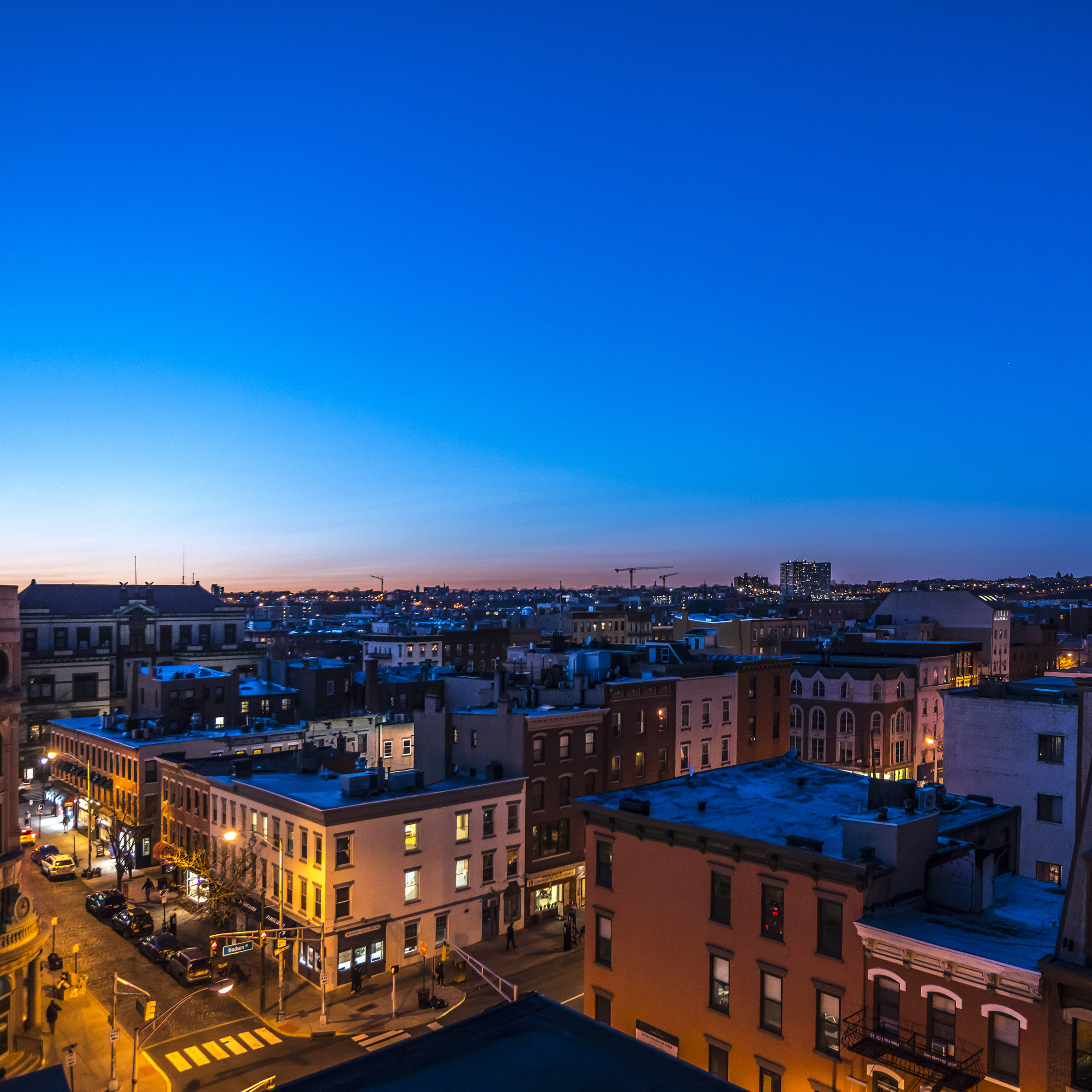 A cityscape at dusk, with buildings lining the streets and a gradient blue sky.