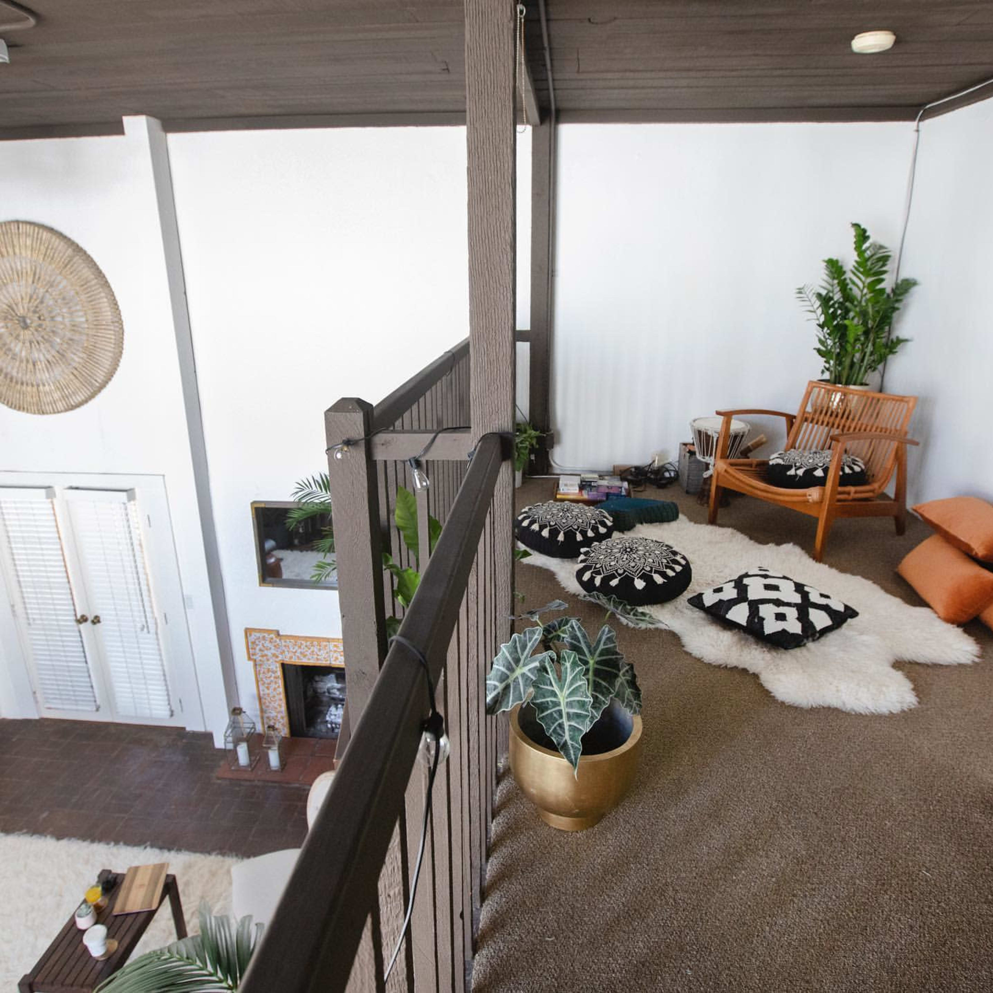 A cozy loft space with a seating area featuring a wooden chair, decorative pillows, a large rug, and several plants.