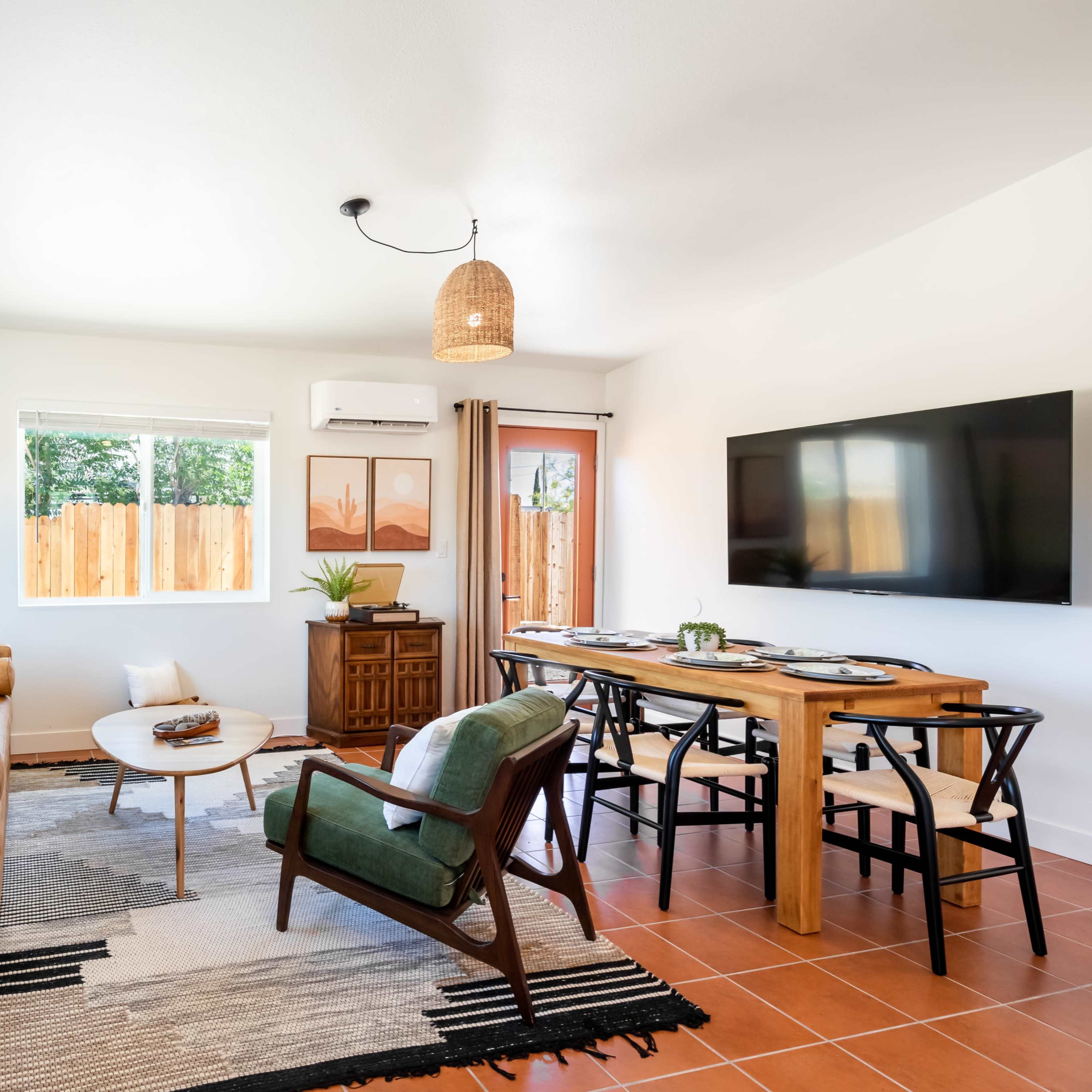 A modern living room features a brown leather sofa, a round coffee table, a dining area with a wooden table, and a large wall-mounted television.