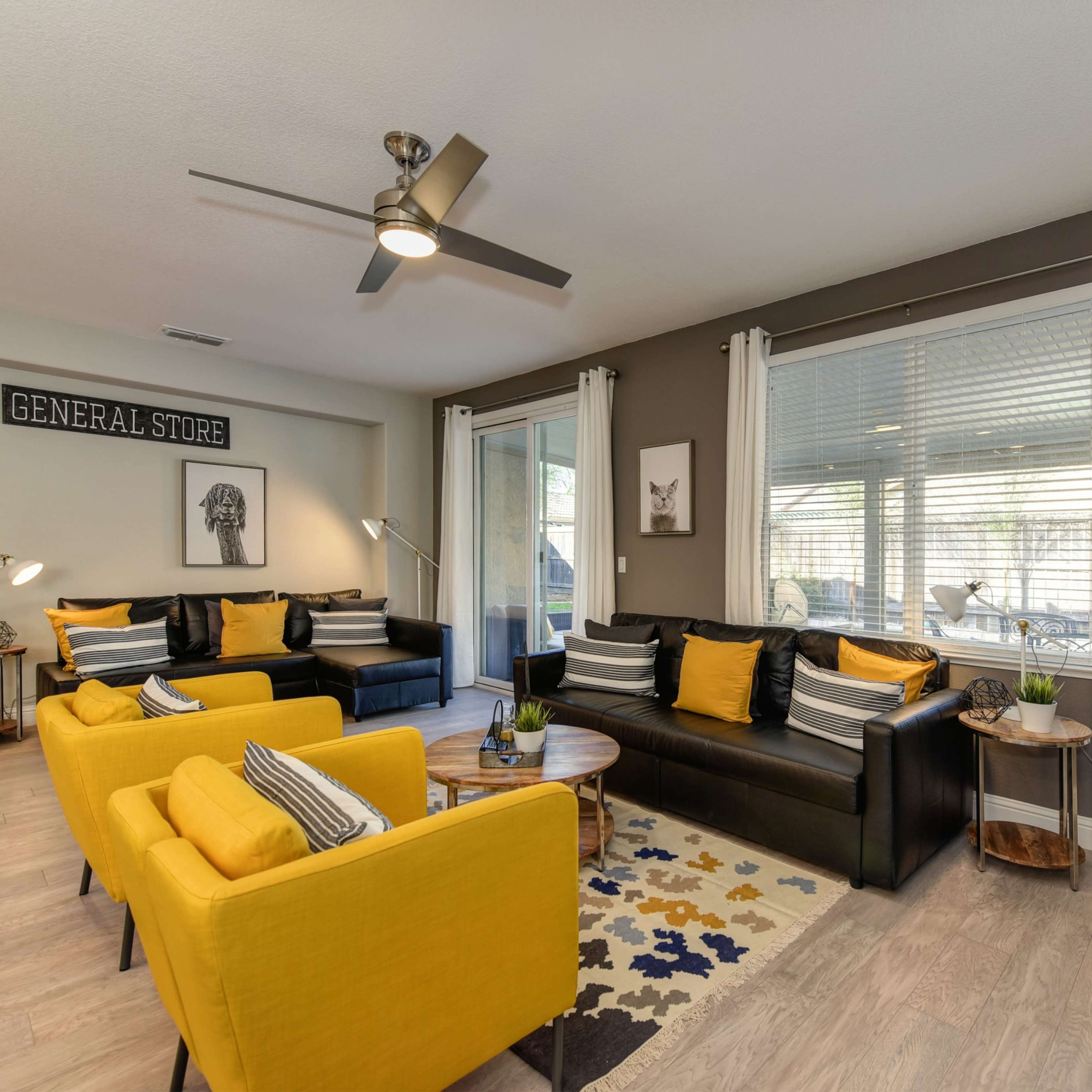 A modern living room features a mix of black and yellow furniture, large windows, and a neutral color scheme with decorative items.