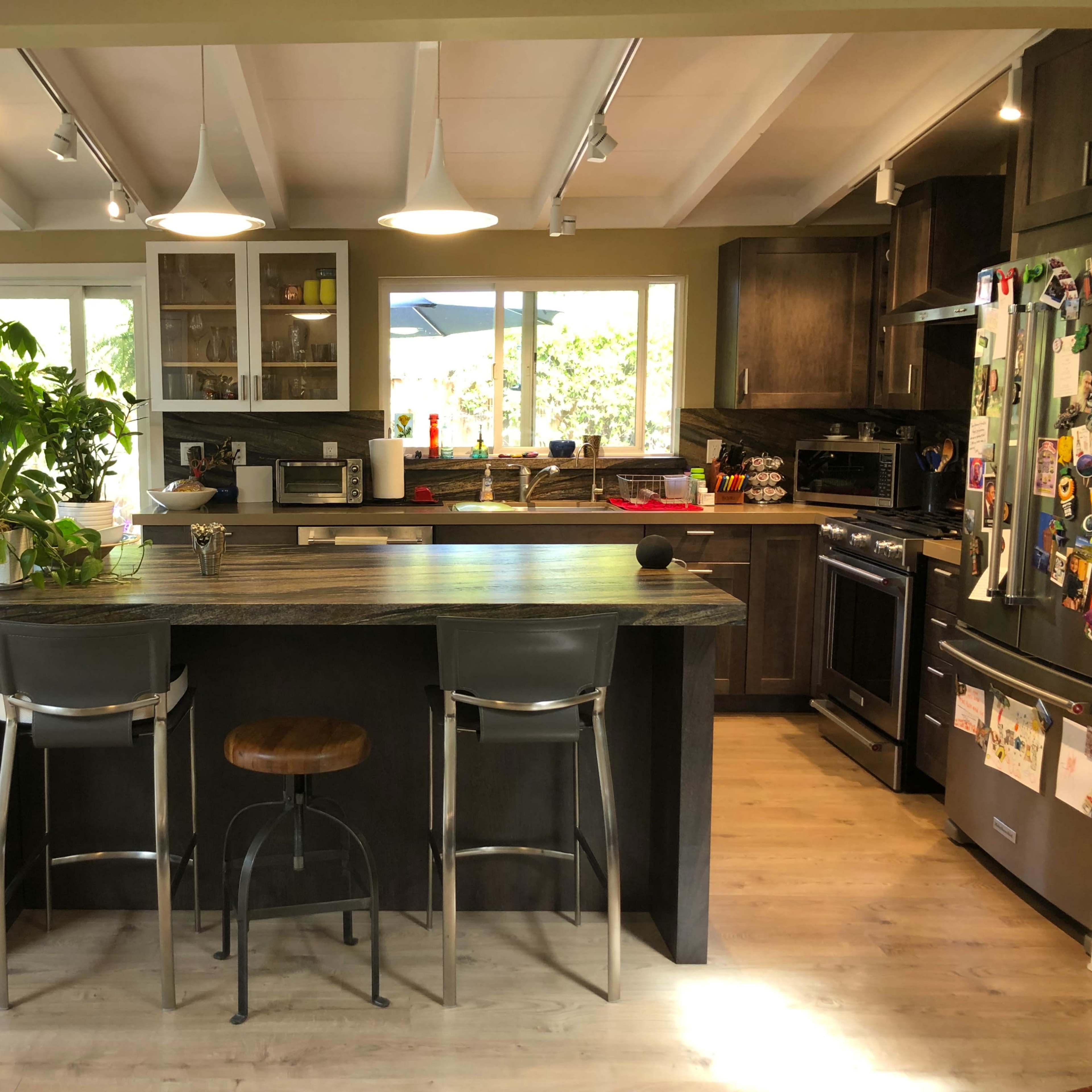 A modern kitchen with a central island, bar stools, and large windows letting in natural light.