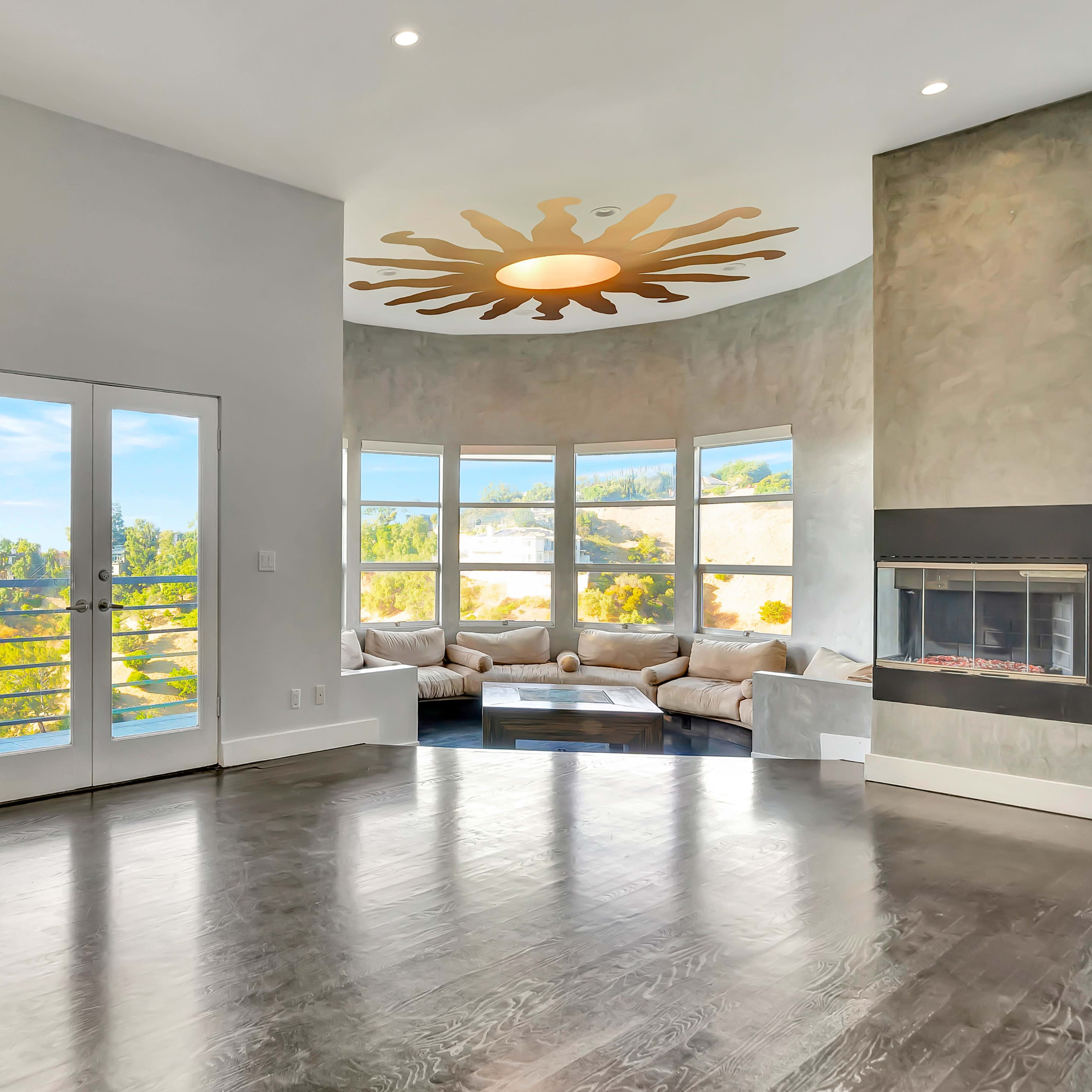 A spacious living room features large windows, a circular ceiling design, a modern fireplace, and access to a patio.