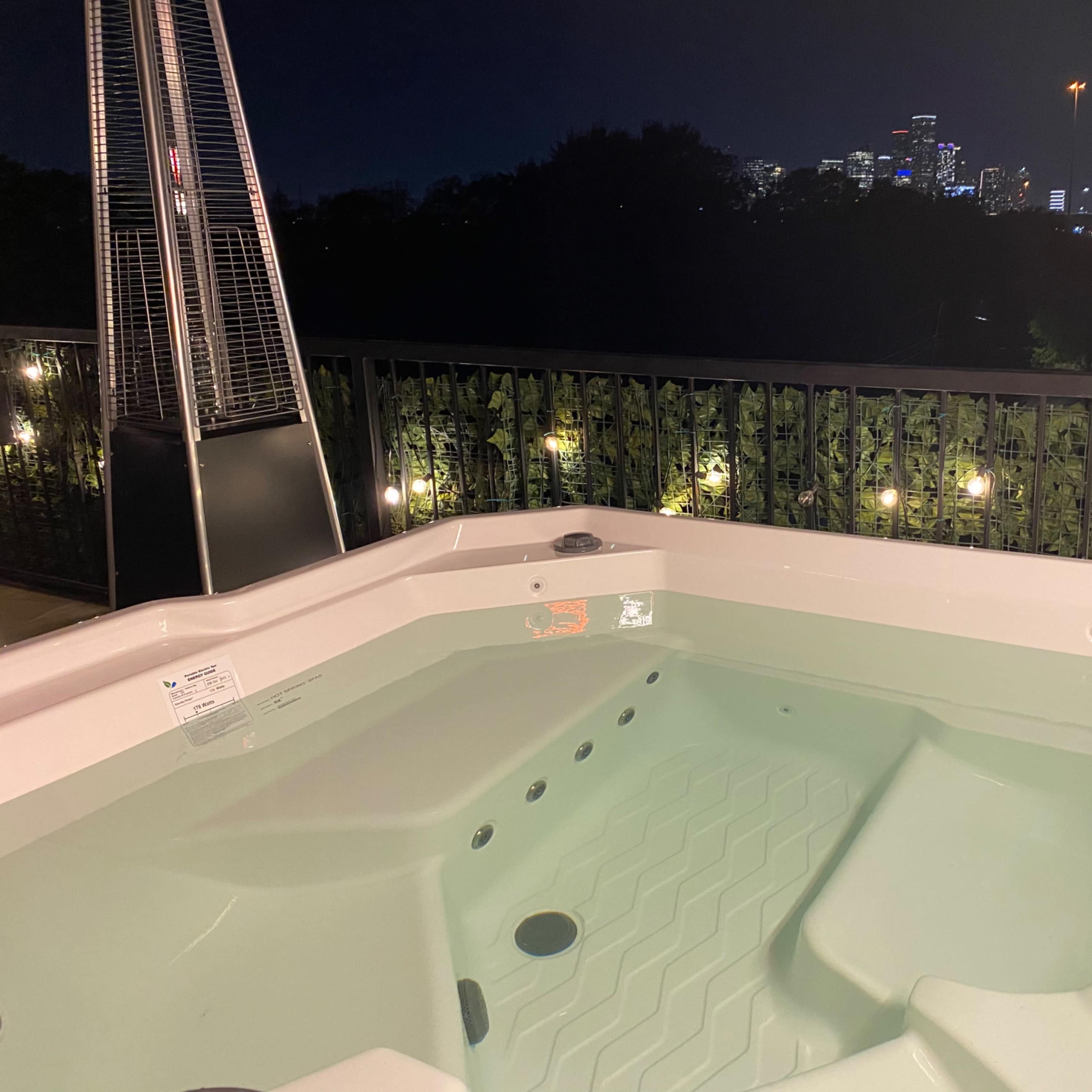 A hot tub filled with water sits on a deck overlooking a city skyline at night.