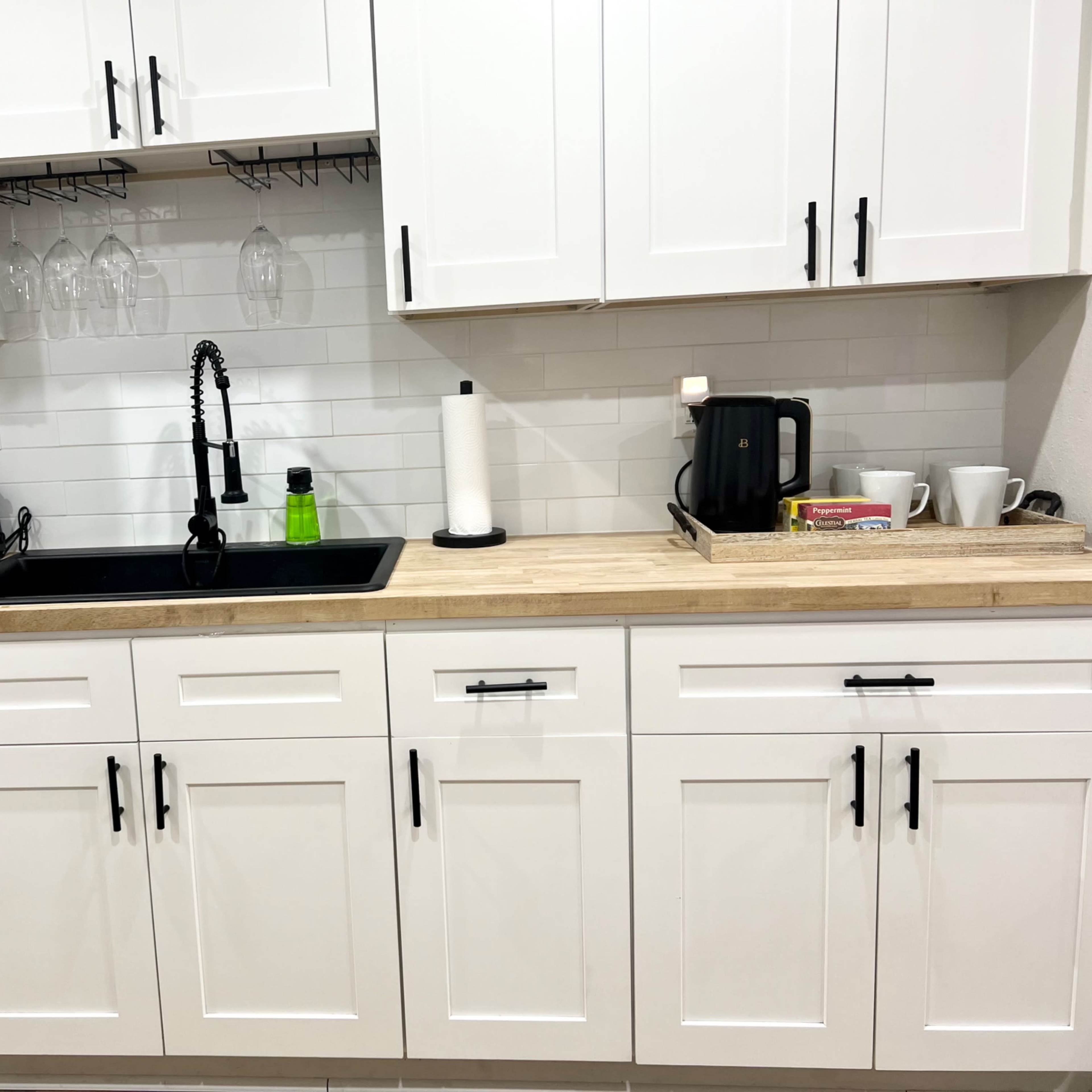 A modern kitchen with white cabinets, a black sink, and a wooden countertop featuring various kitchen appliances and utensils.
