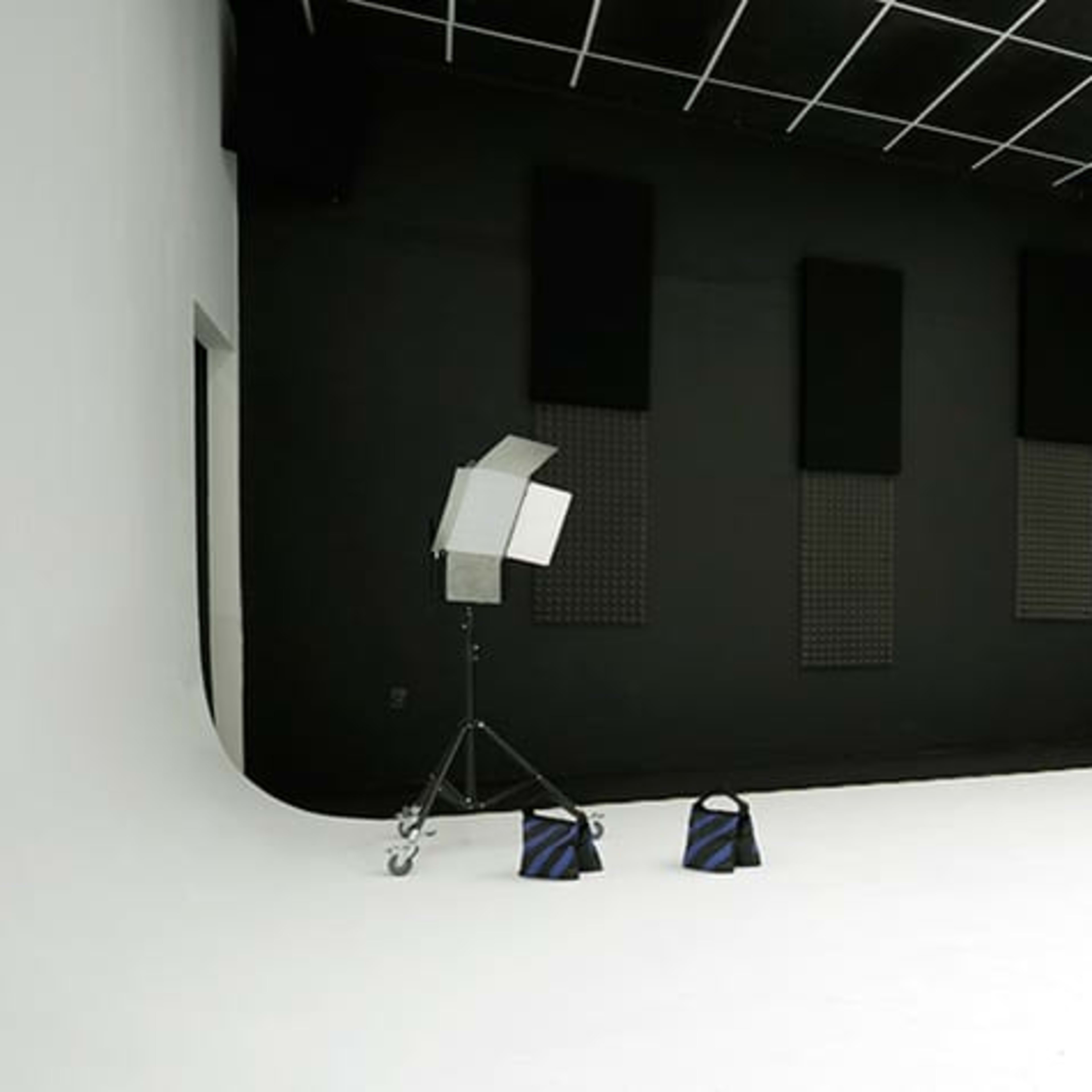 A spacious photo studio with a white backdrop, black walls, and various lighting equipment set up in the corner.
