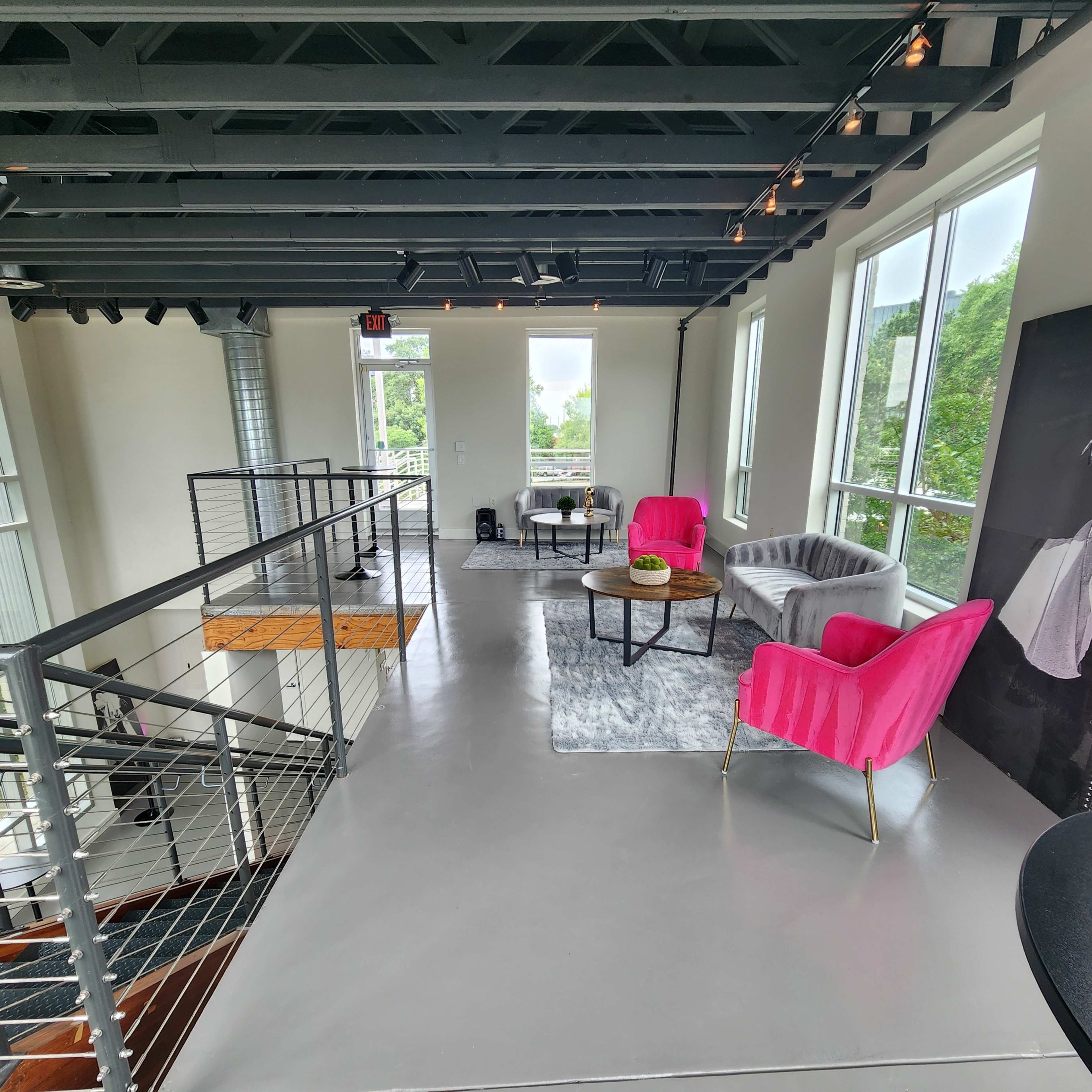 A modern, well-lit interior space featuring pink and gray seating, large windows, and a staircase.