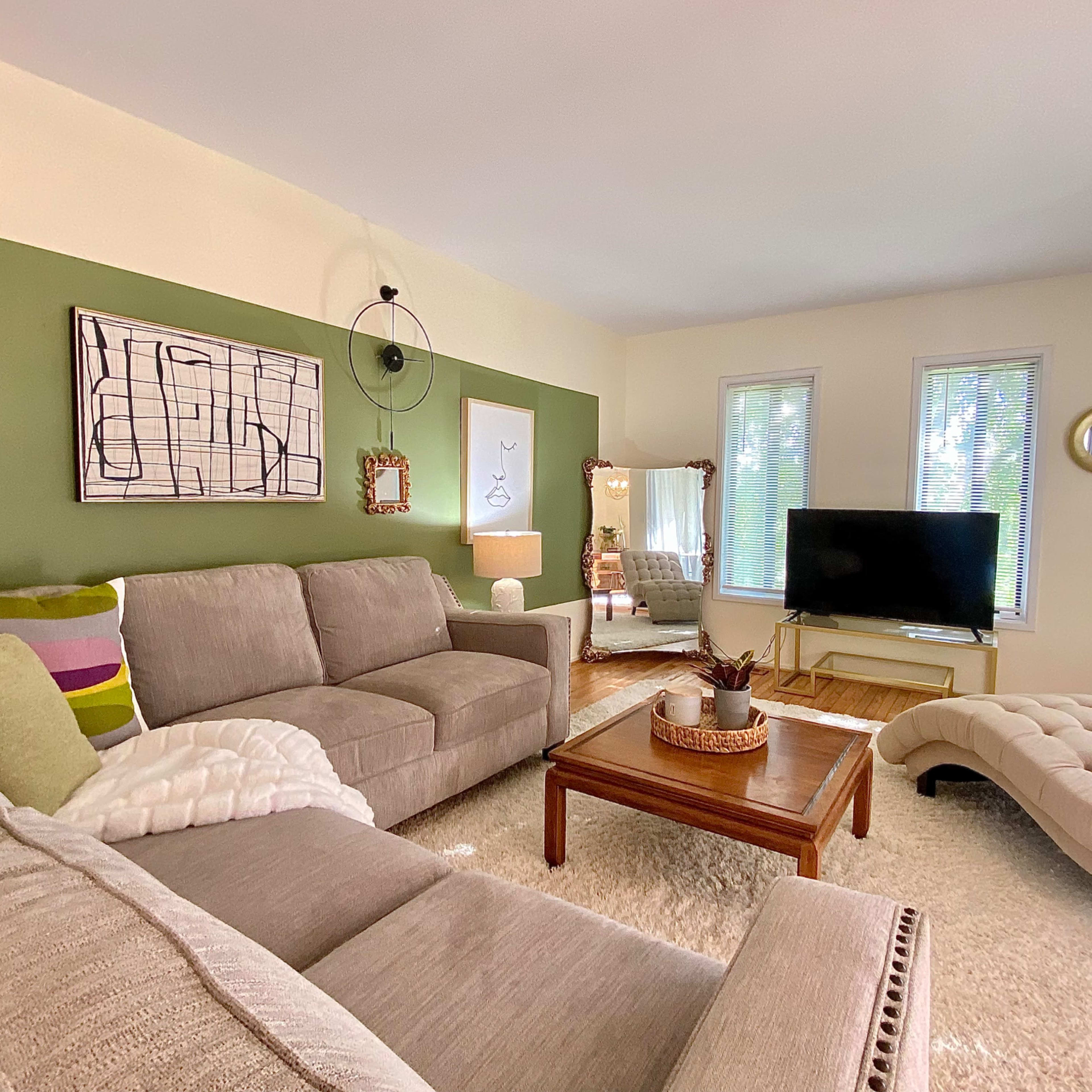 A living room with a sectional sofa, a coffee table, a television on a stand, and large windows letting in natural light.