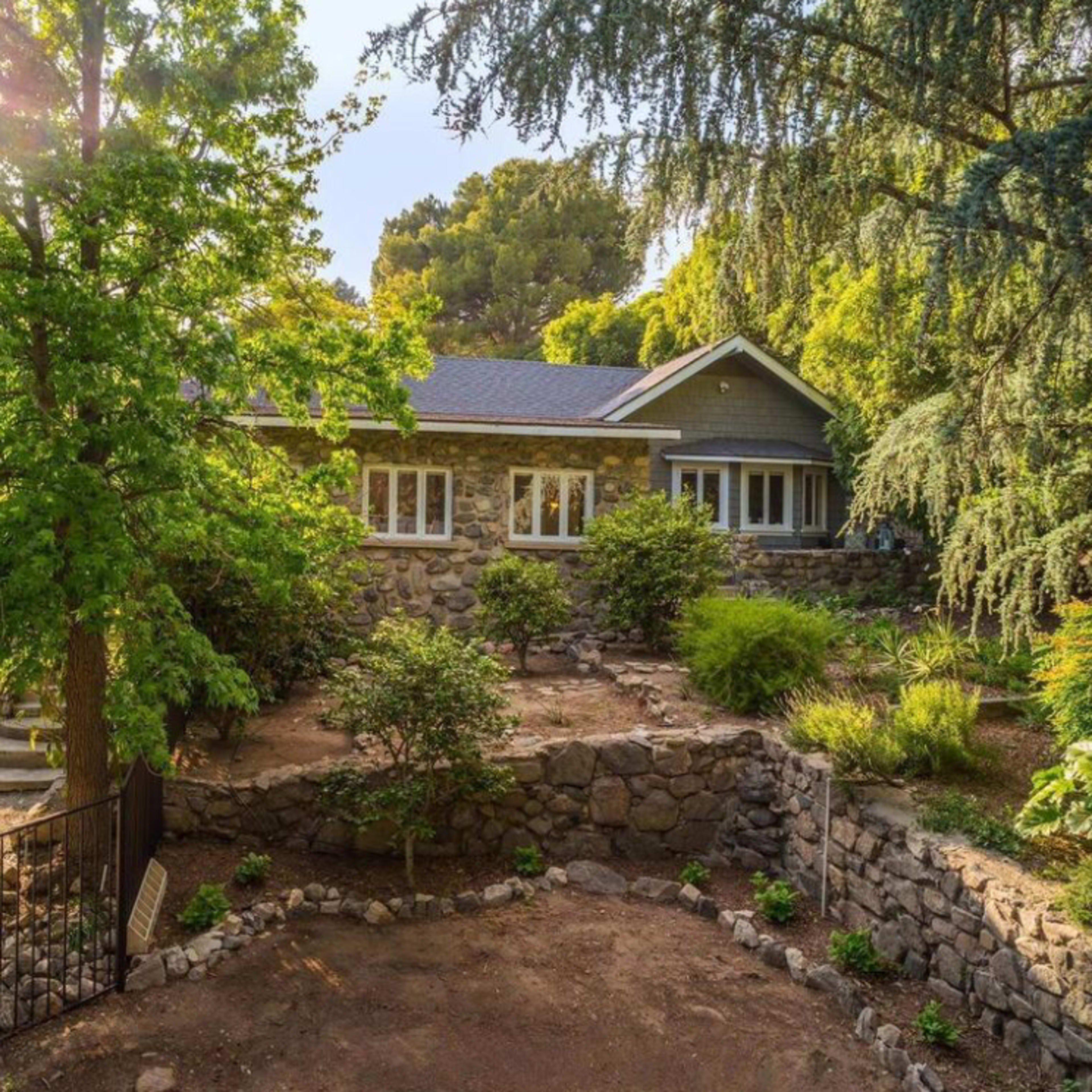 A stone-faced house is nestled among lush greenery and trees in a well-maintained garden setting.