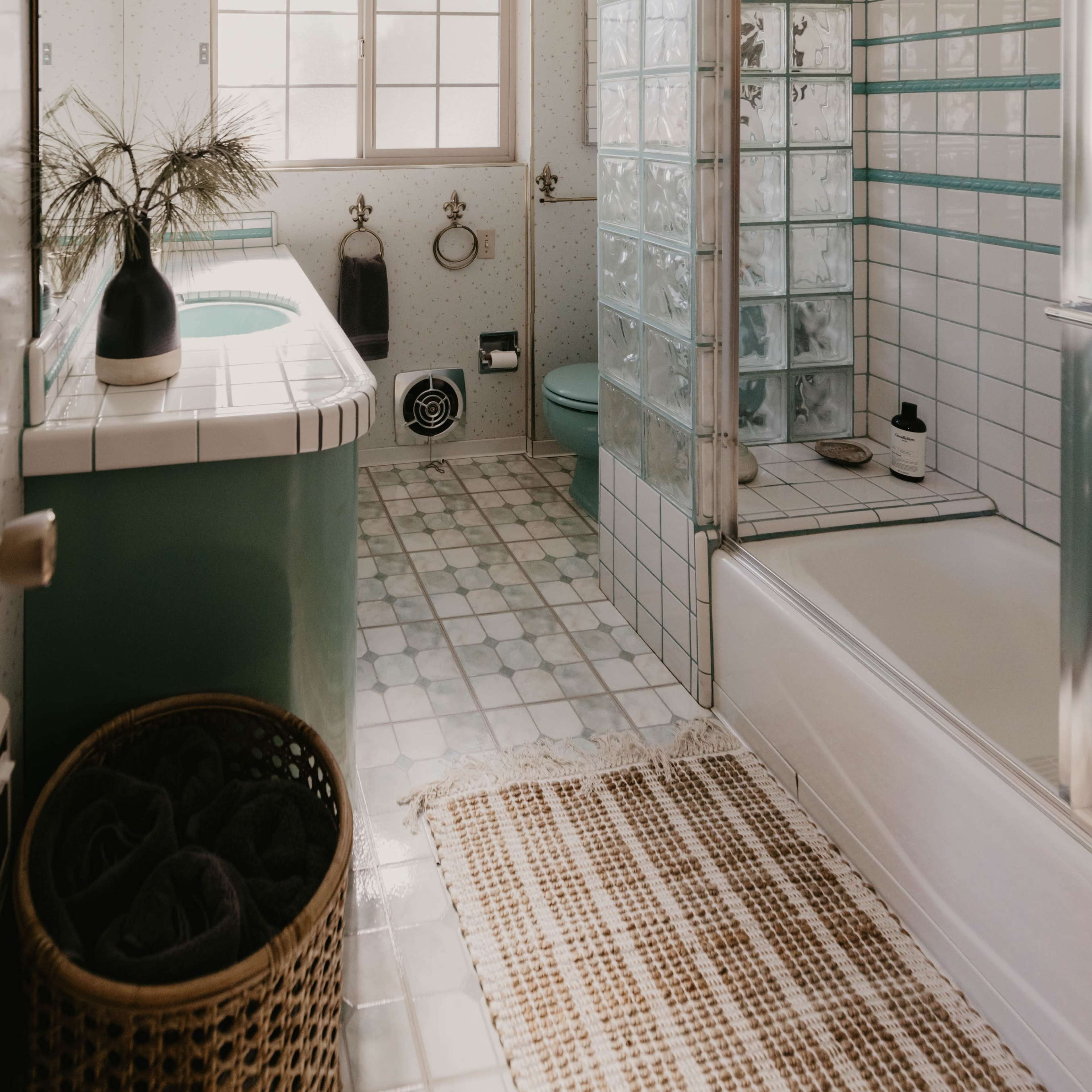 A bathroom features a glass shower, a bathtub, a sink with a plant, and tiled walls and floors.