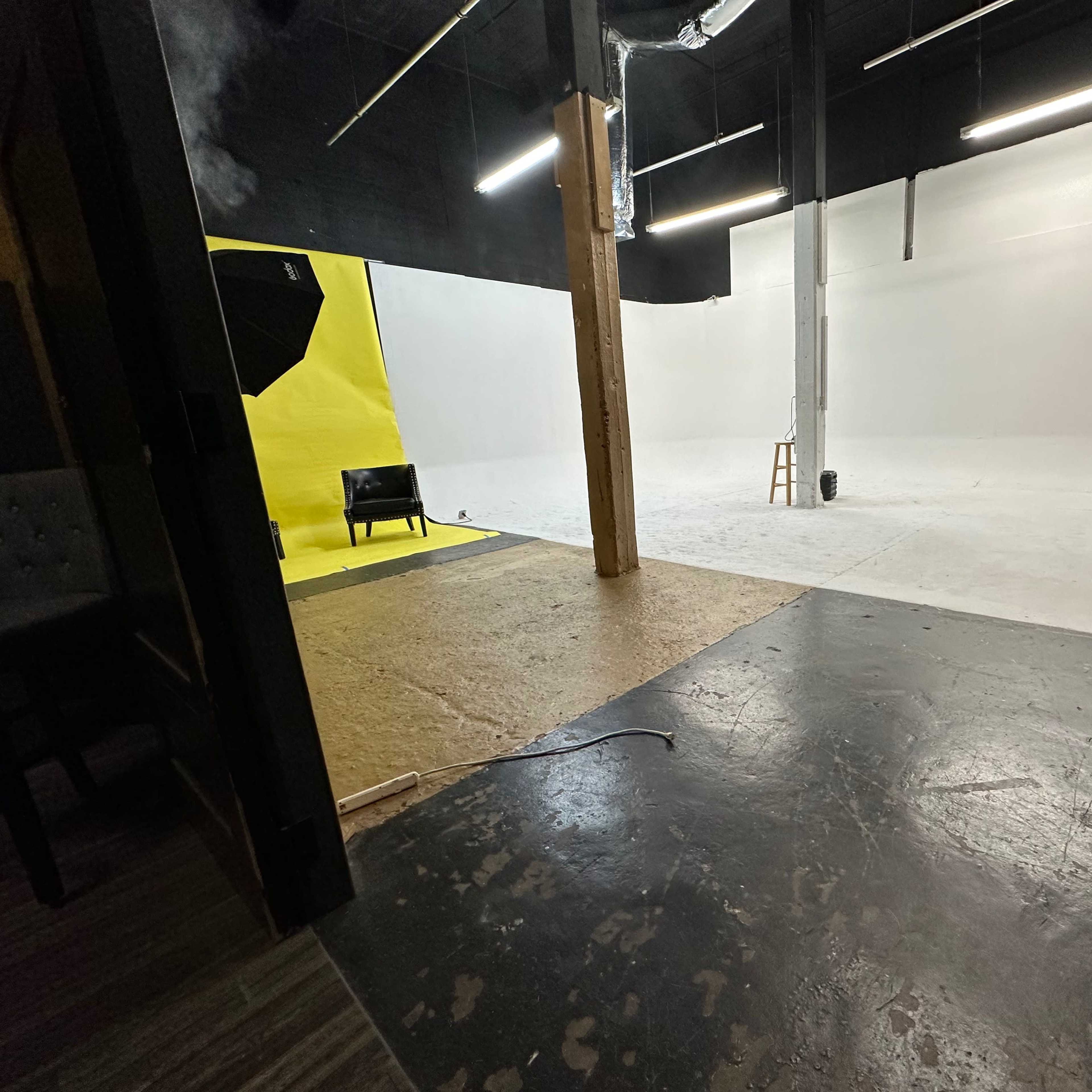 A spacious photography studio divided by a wooden beam, featuring a white backdrop on one side and a yellow backdrop on the other.