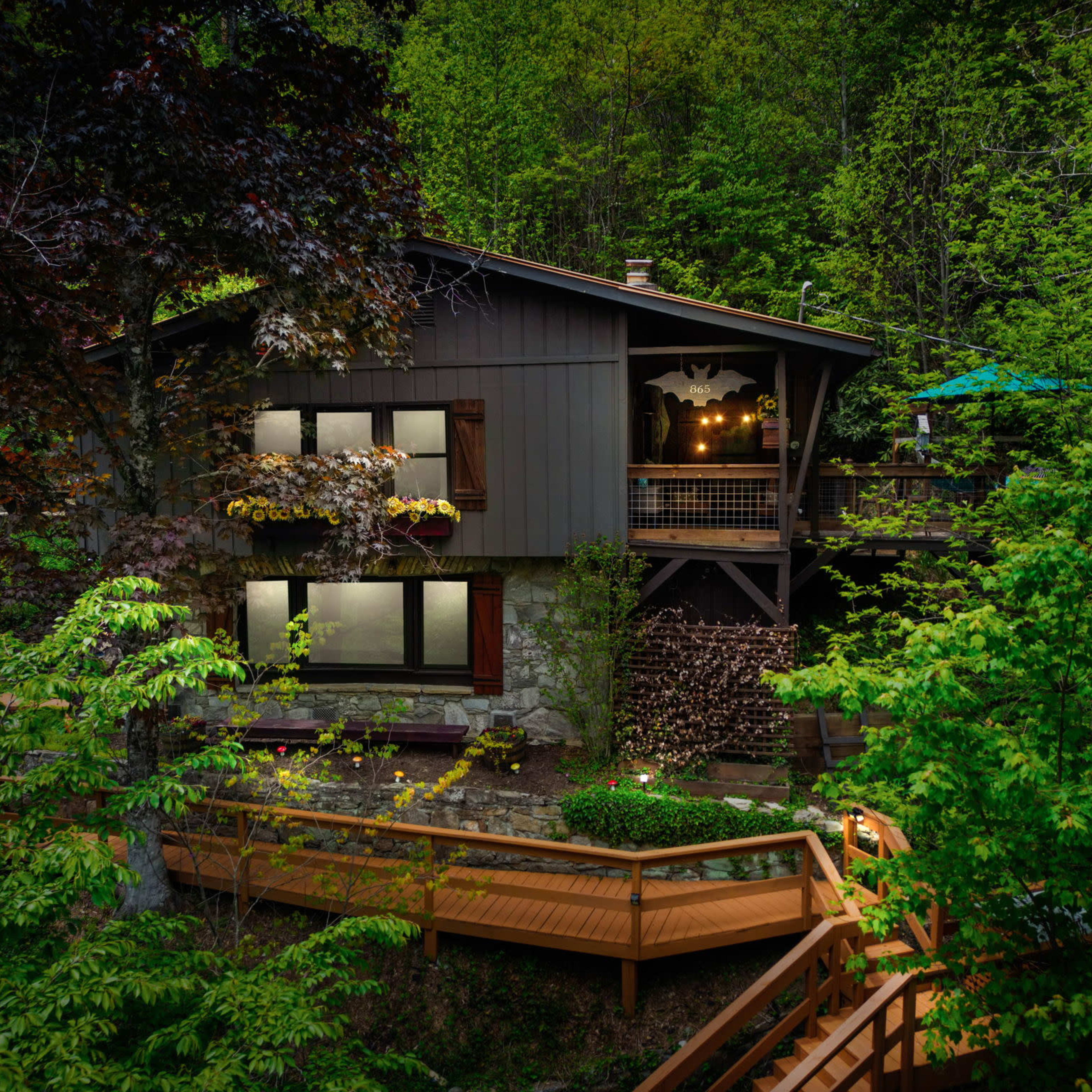 A wooden house with large windows sits nestled among trees, featuring a deck and outdoor seating.