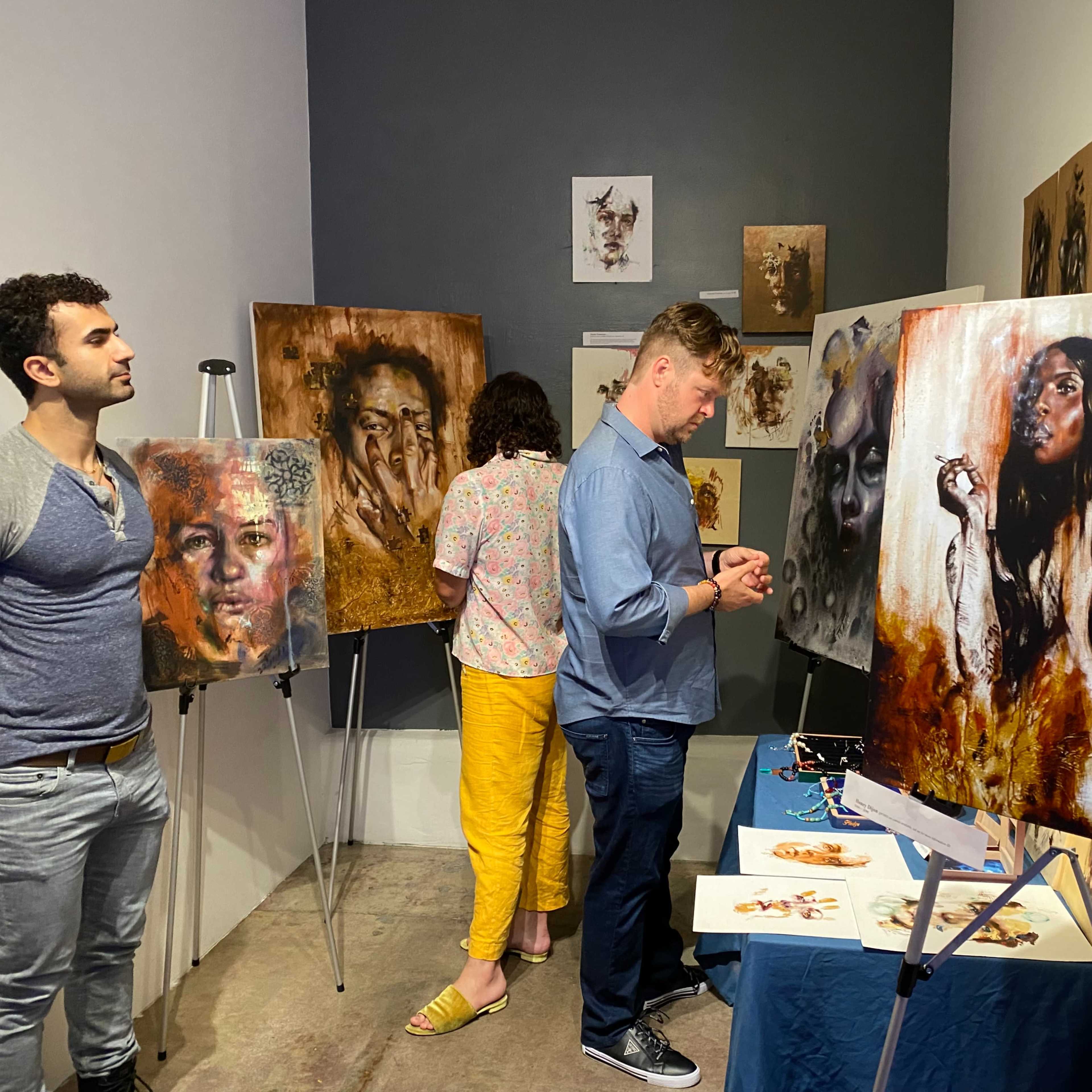 A small art gallery features several expressive paintings on the walls, with three individuals engaged in observing the artwork.