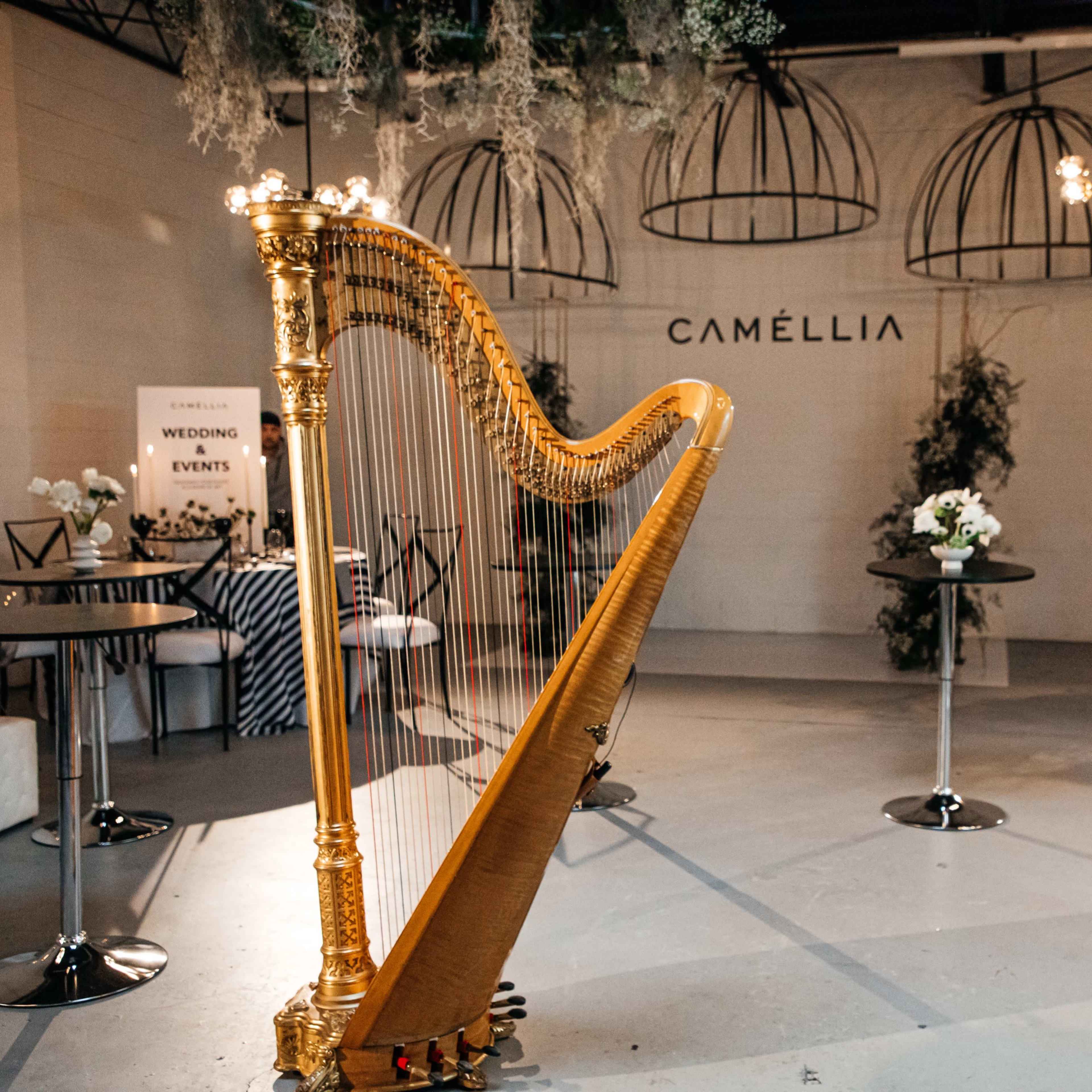 A gold harp stands prominently in a well-lit event space, surrounded by tables adorned with floral arrangements.