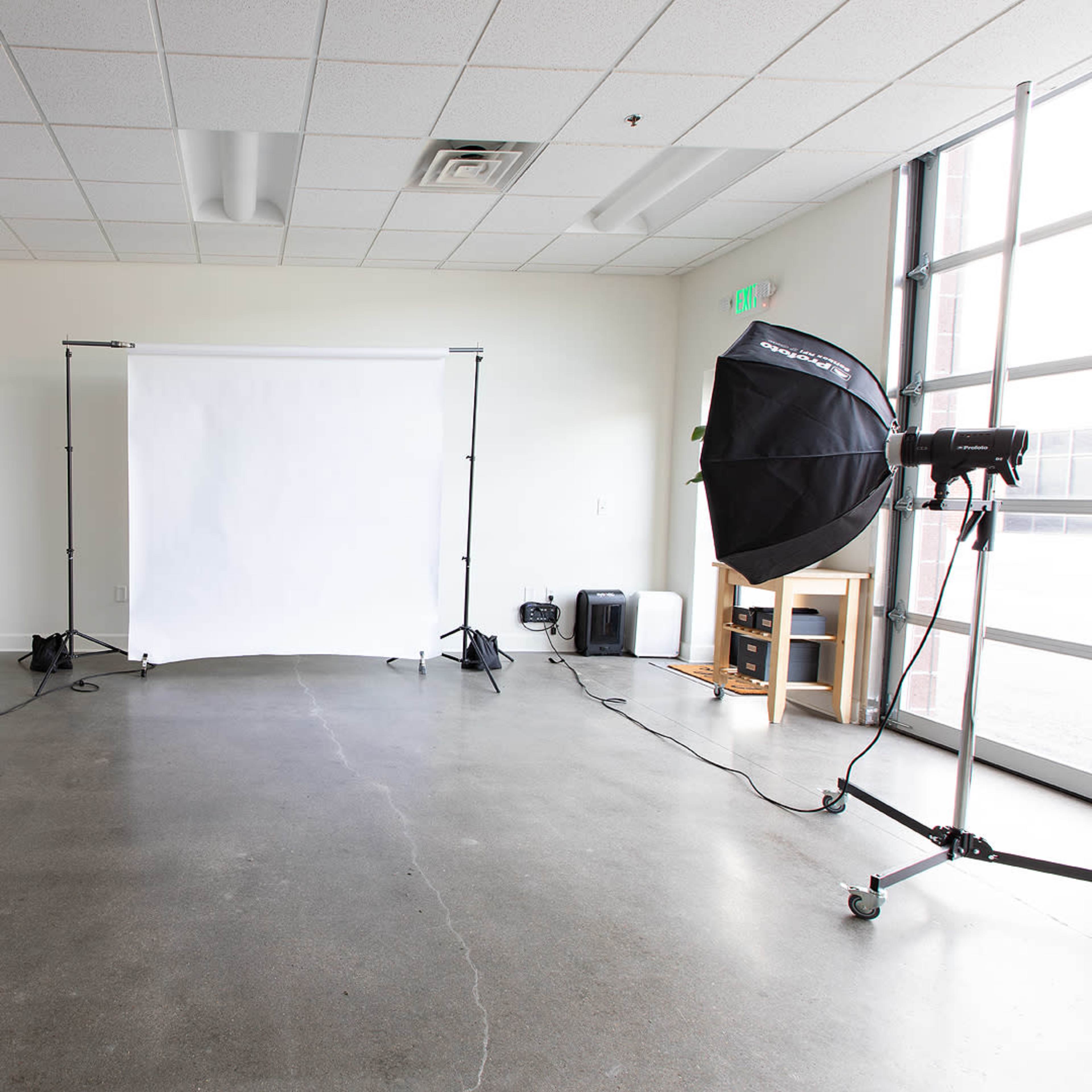 A photography studio is set up with two large softbox lights facing a backdrop on a stand in a spacious room.
