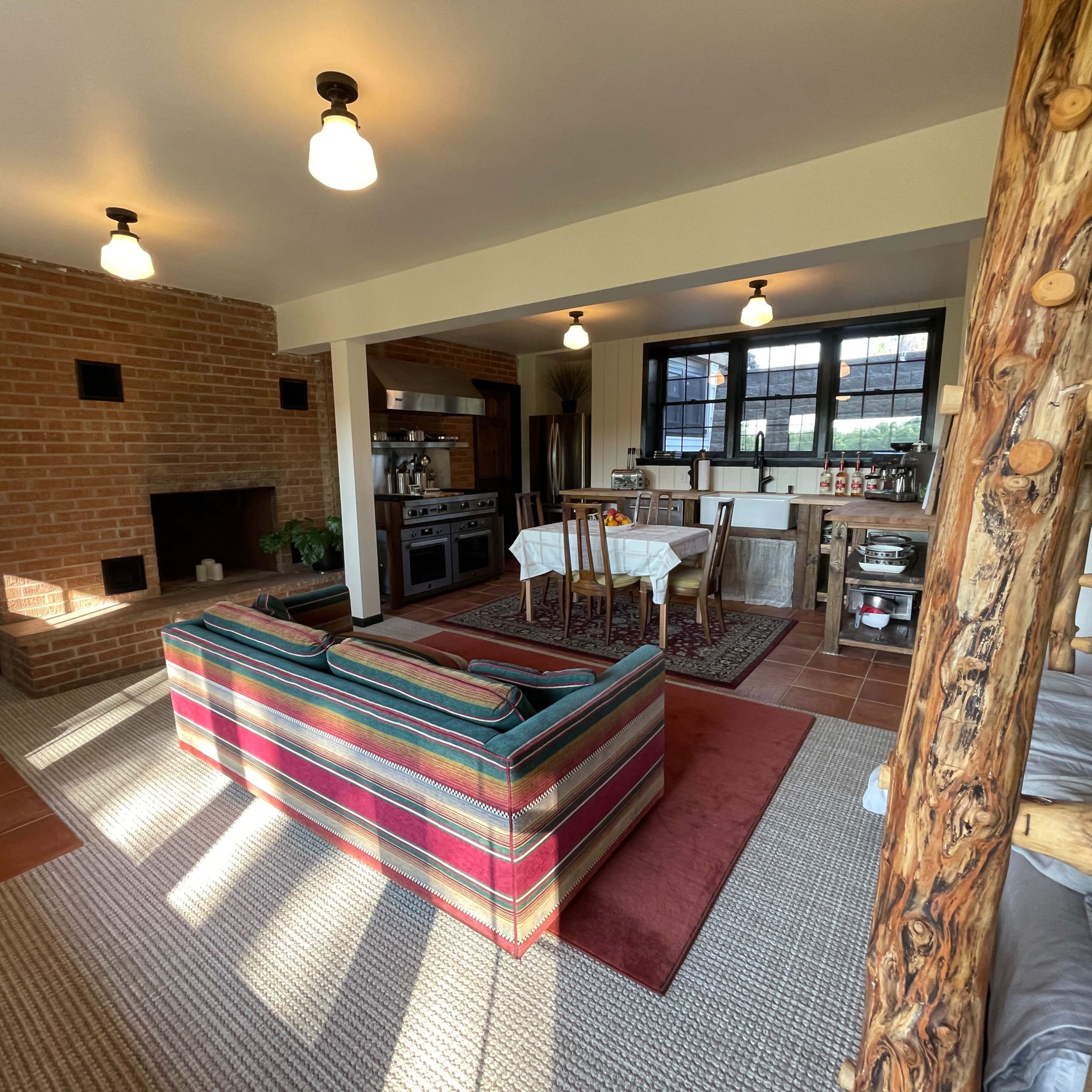 A cozy living space featuring a striped sofa, a brick fireplace, a wooden dining area, and a kitchen in an open-concept layout.