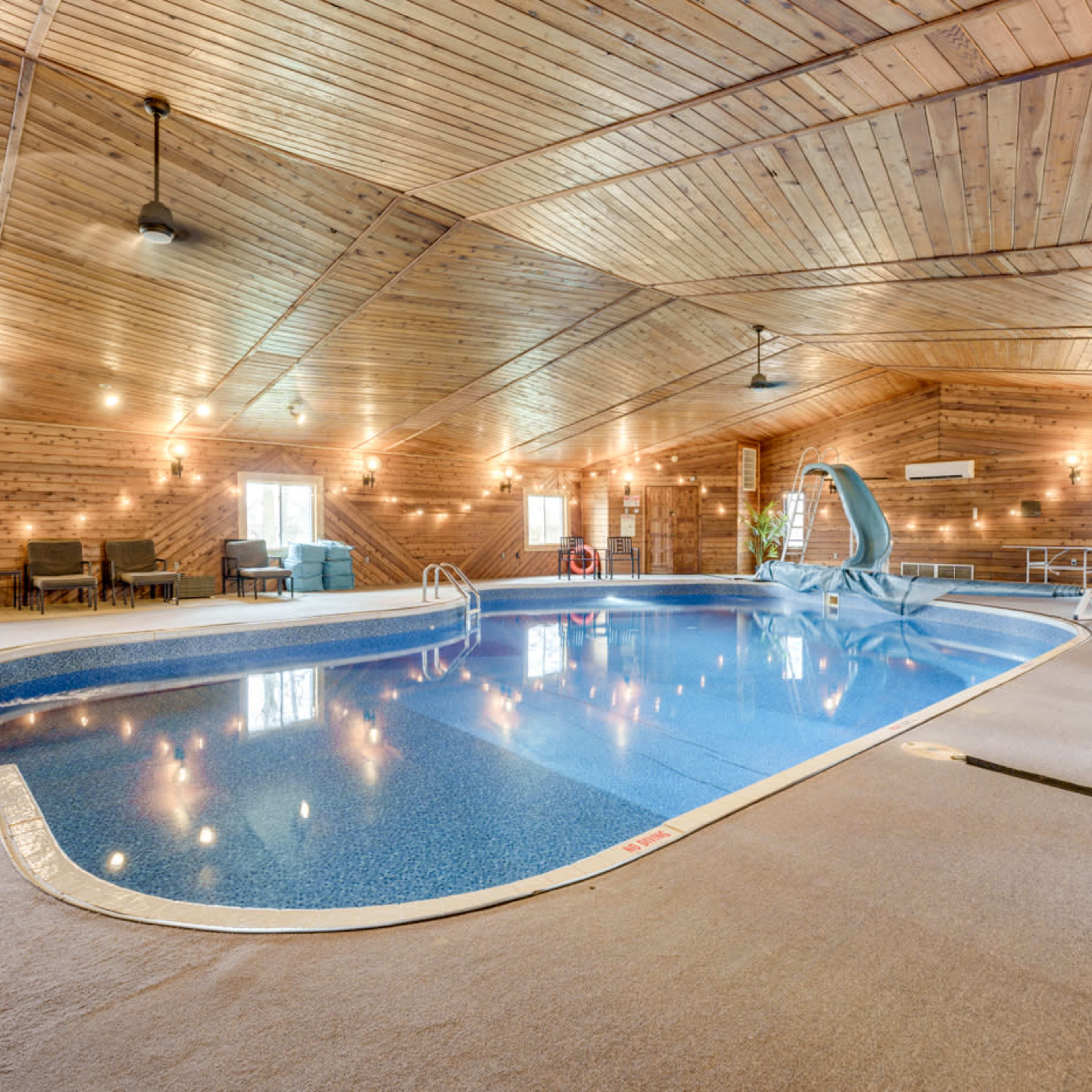 An indoor swimming pool area with a wooden ceiling, bright lighting, and a water slide.