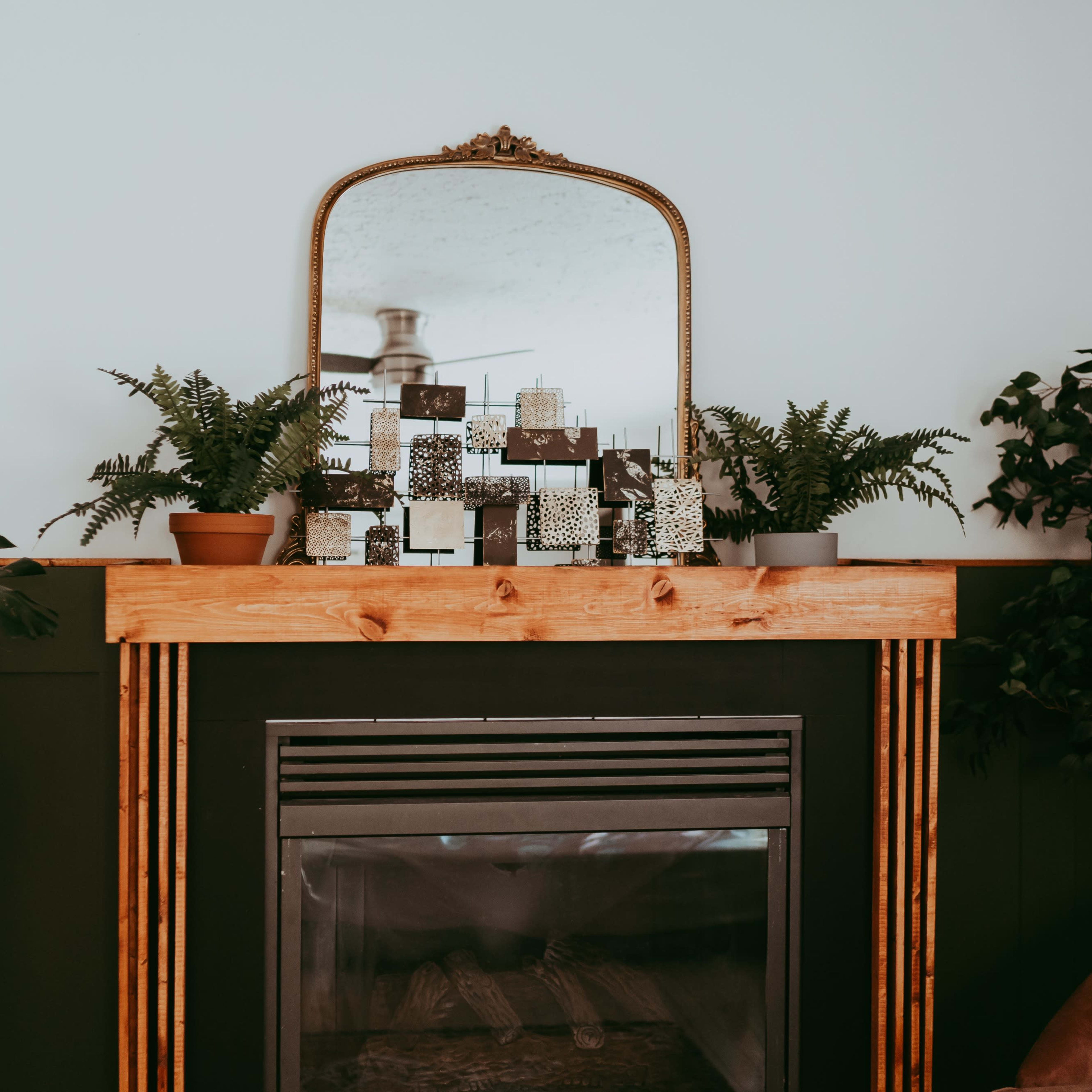 A fireplace mantel is adorned with plants and decorative items, and a mirror hangs above it.