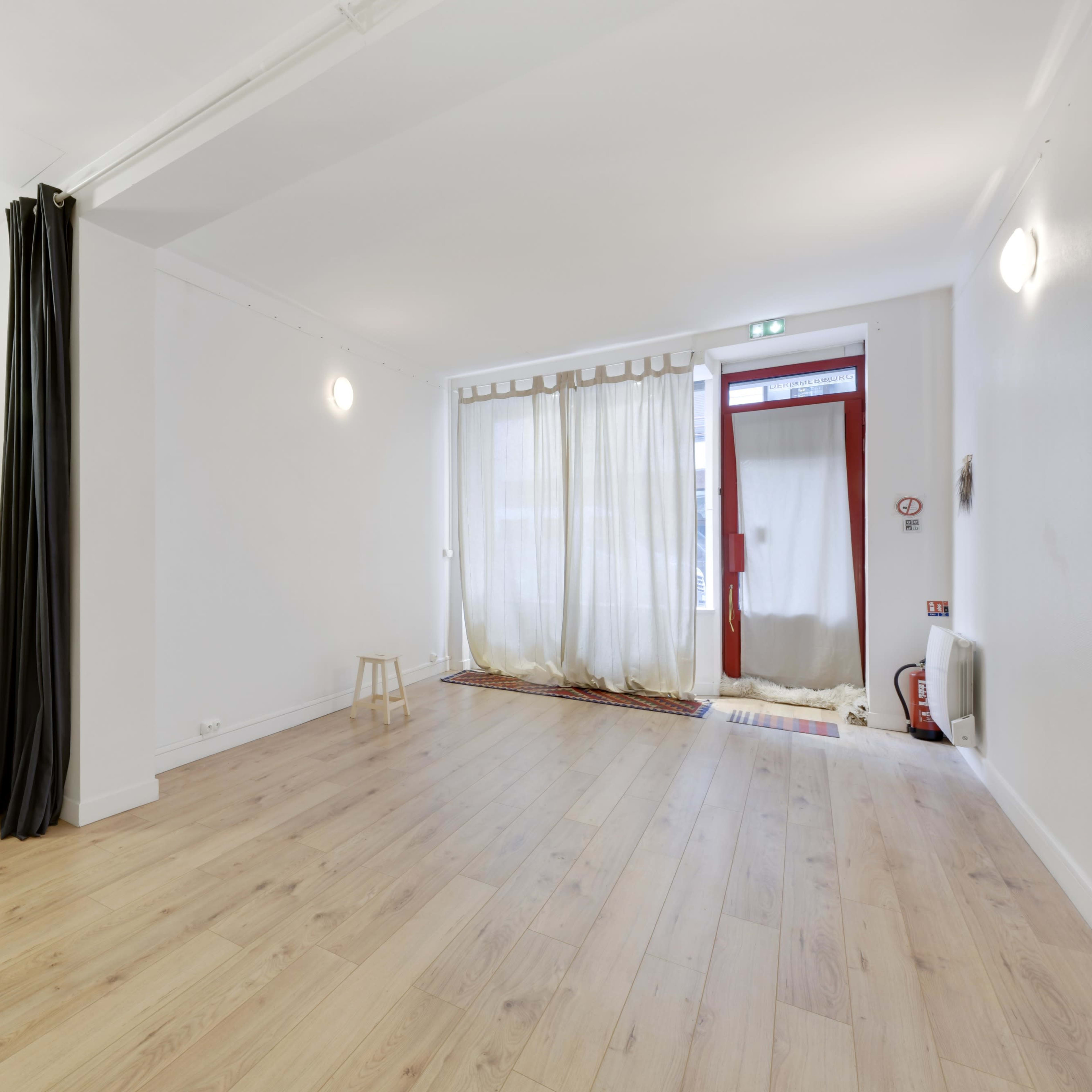 A spacious, minimally furnished room with wooden flooring, a bench along one wall, and sheer curtains covering a doorway.