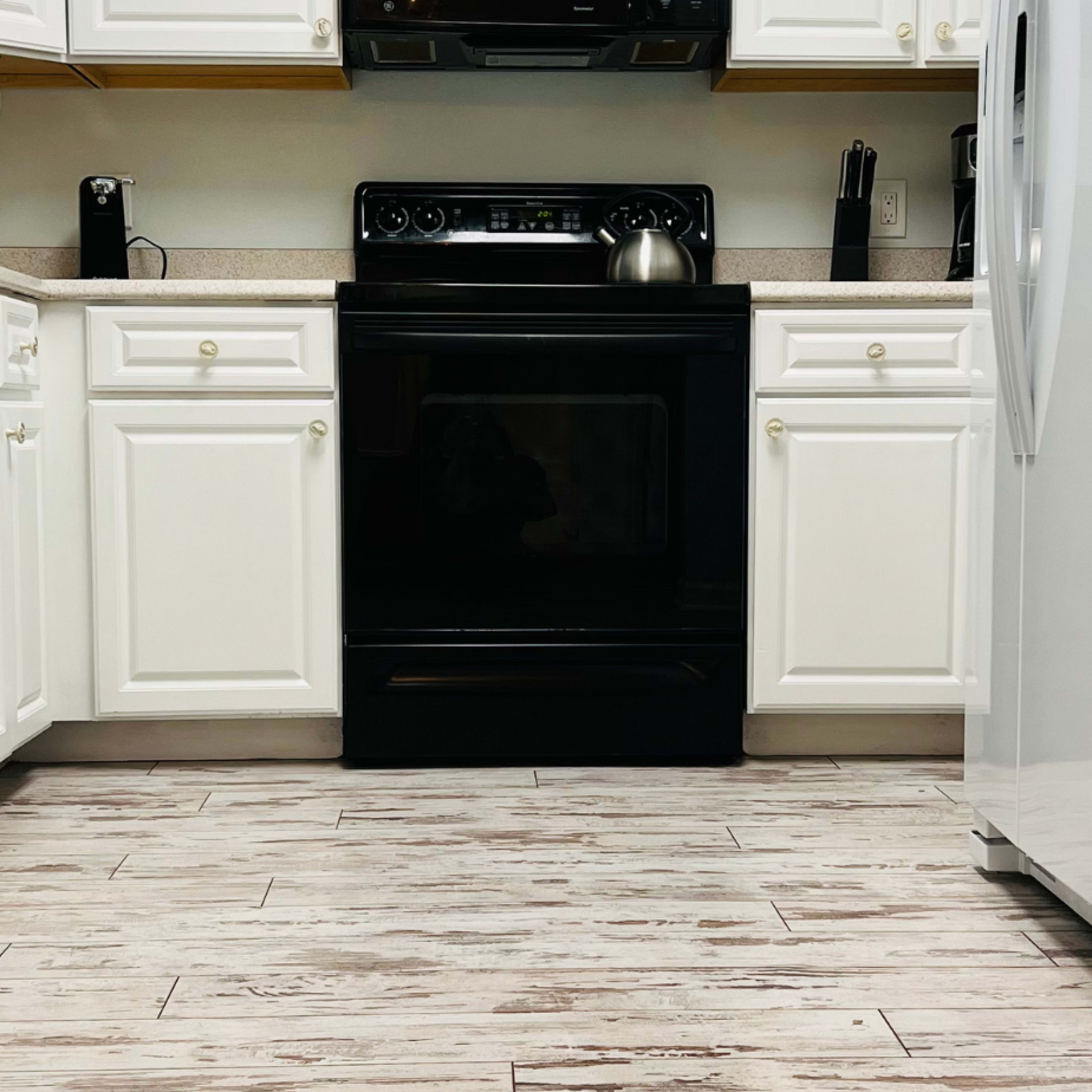 A kitchen features white cabinetry, a black stove, and a stainless steel refrigerator on a wood-patterned floor.