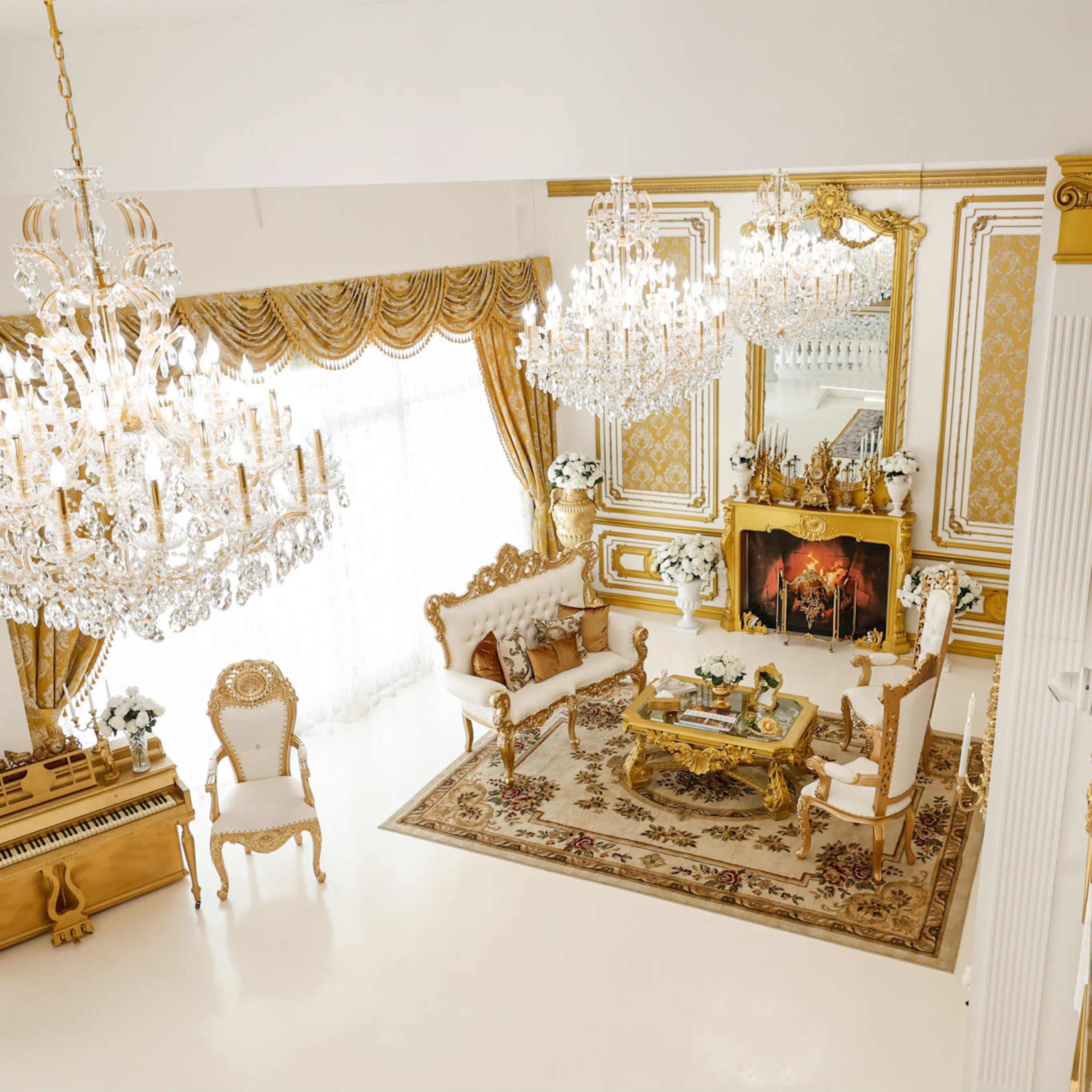 An elegantly decorated living room with golden accents, multiple chandeliers, and a lavish seating arrangement centered around a coffee table.