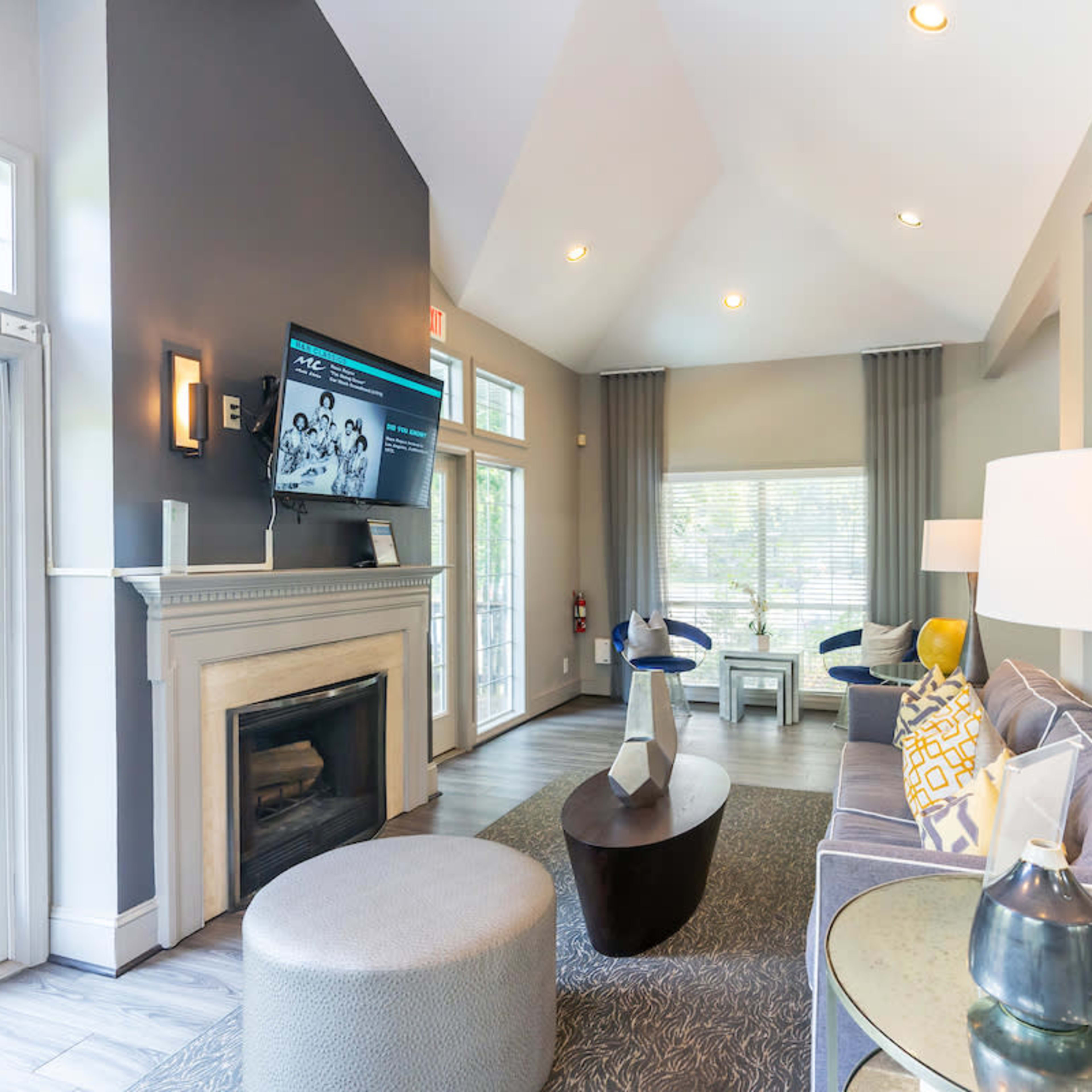 A modern lounge area with a fireplace, large windows, a television mounted on the wall, and comfortable seating arrangements.