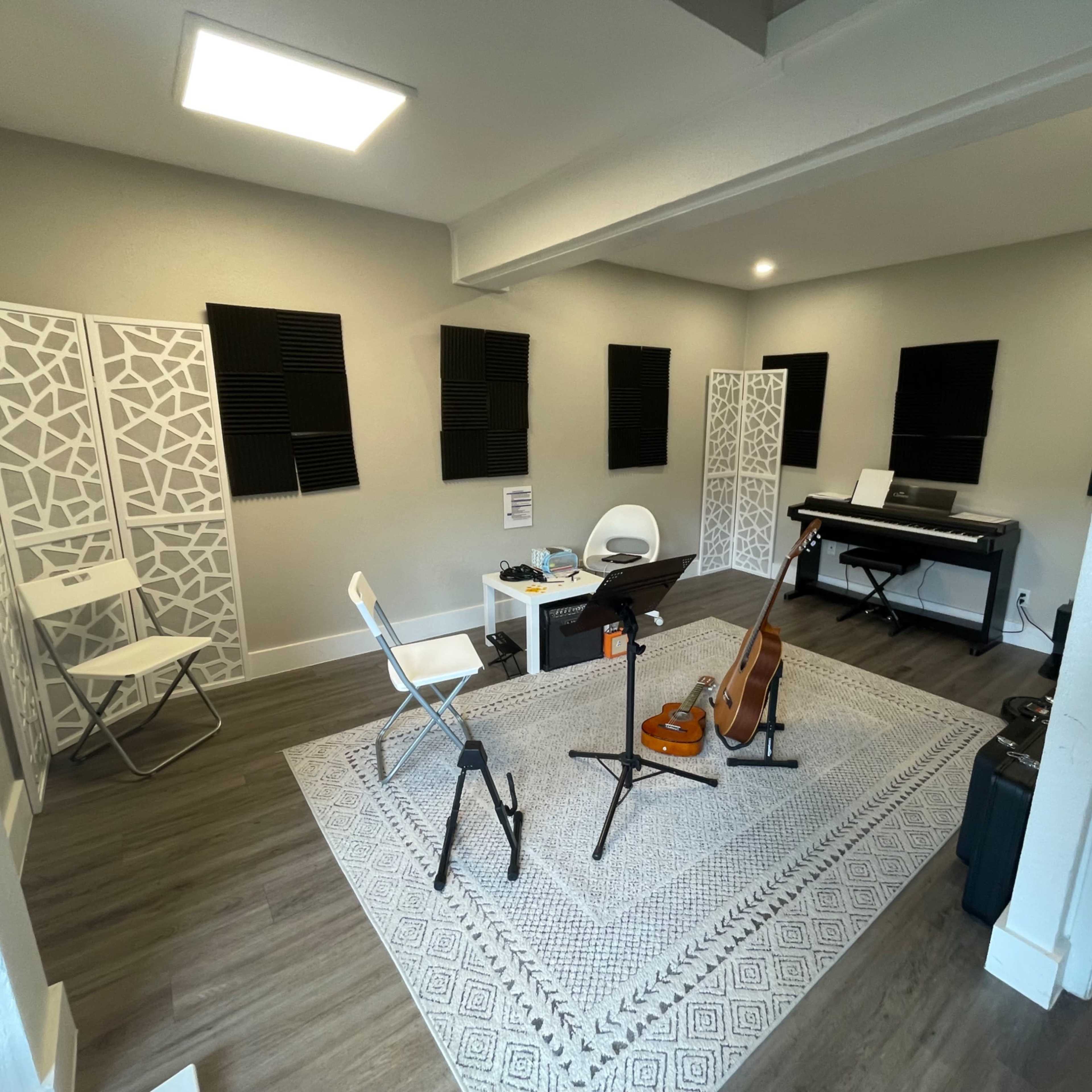 A music practice room with a rug, chairs, a guitar, and a keyboard set against soundproofed walls.