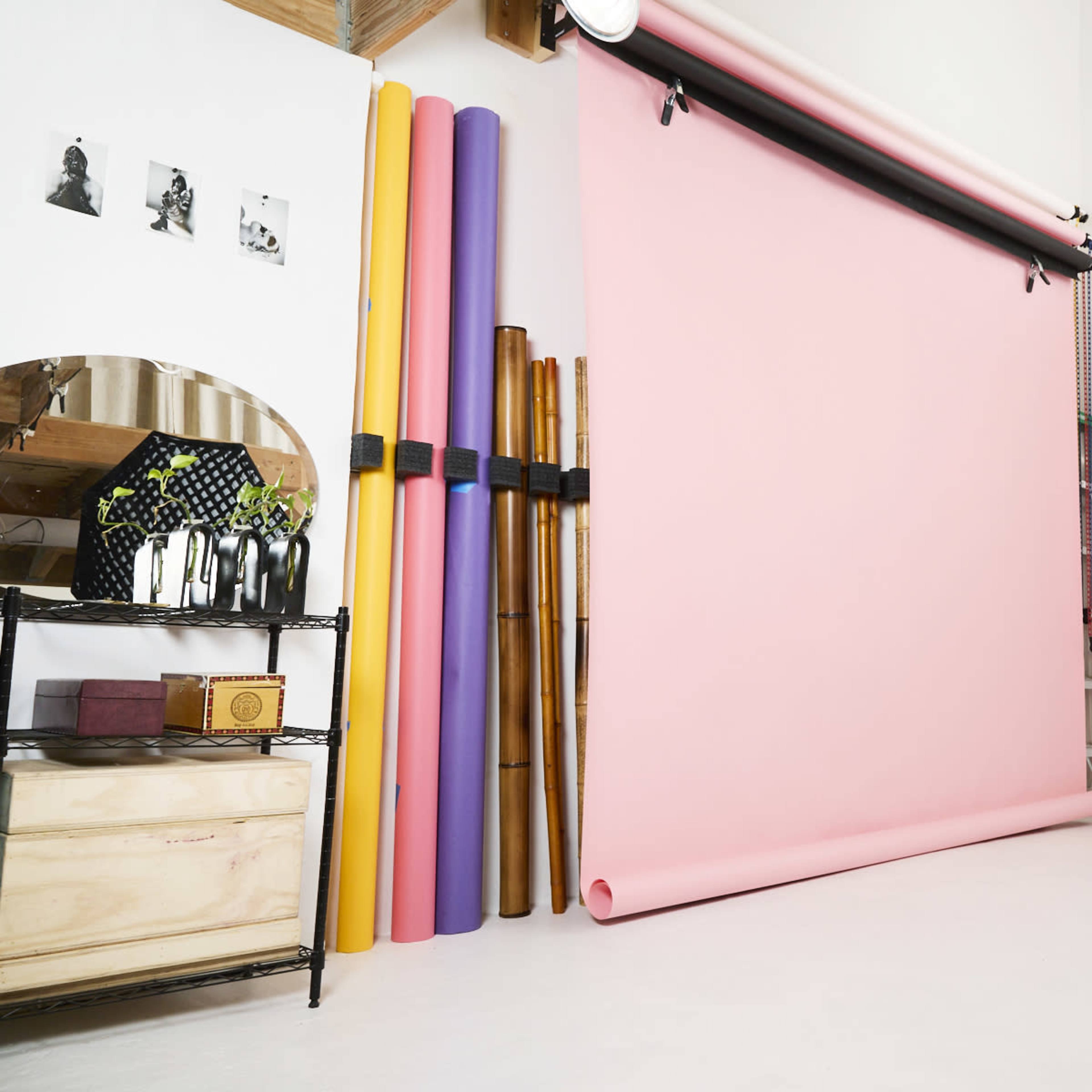 A studio setup with a pink backdrop, various colored rolls of paper, a mirror, and a closed door.
