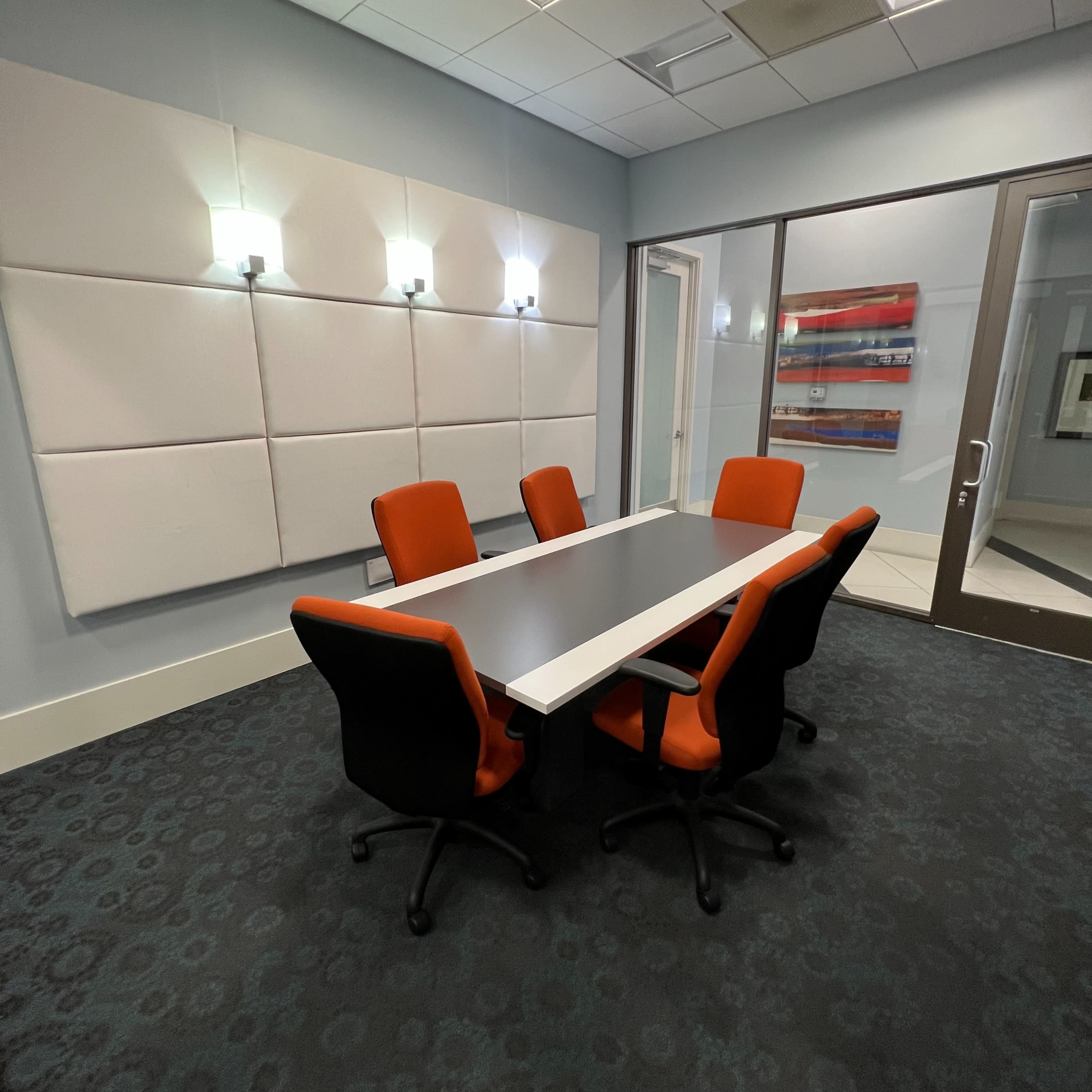 A modern conference room features a rectangular table surrounded by five chairs, with wall panels and decorative lighting.