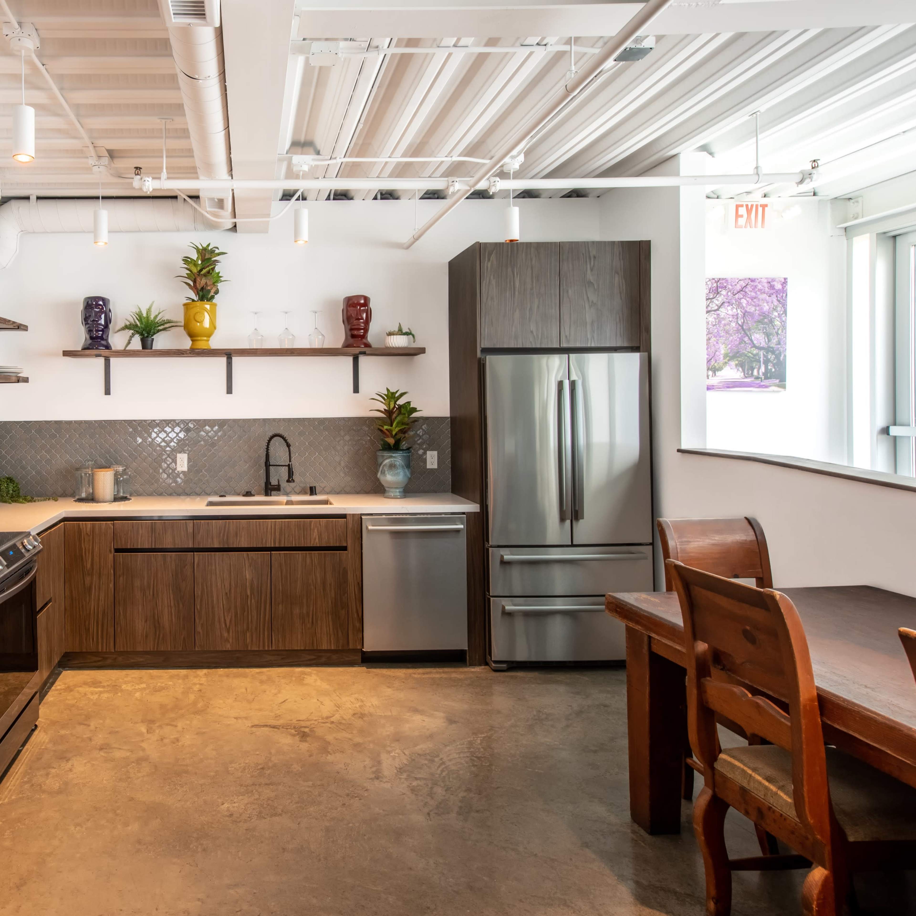 A modern kitchen features wooden cabinets, a stainless steel refrigerator, and a dining table, with various decorative items displayed on the shelves.