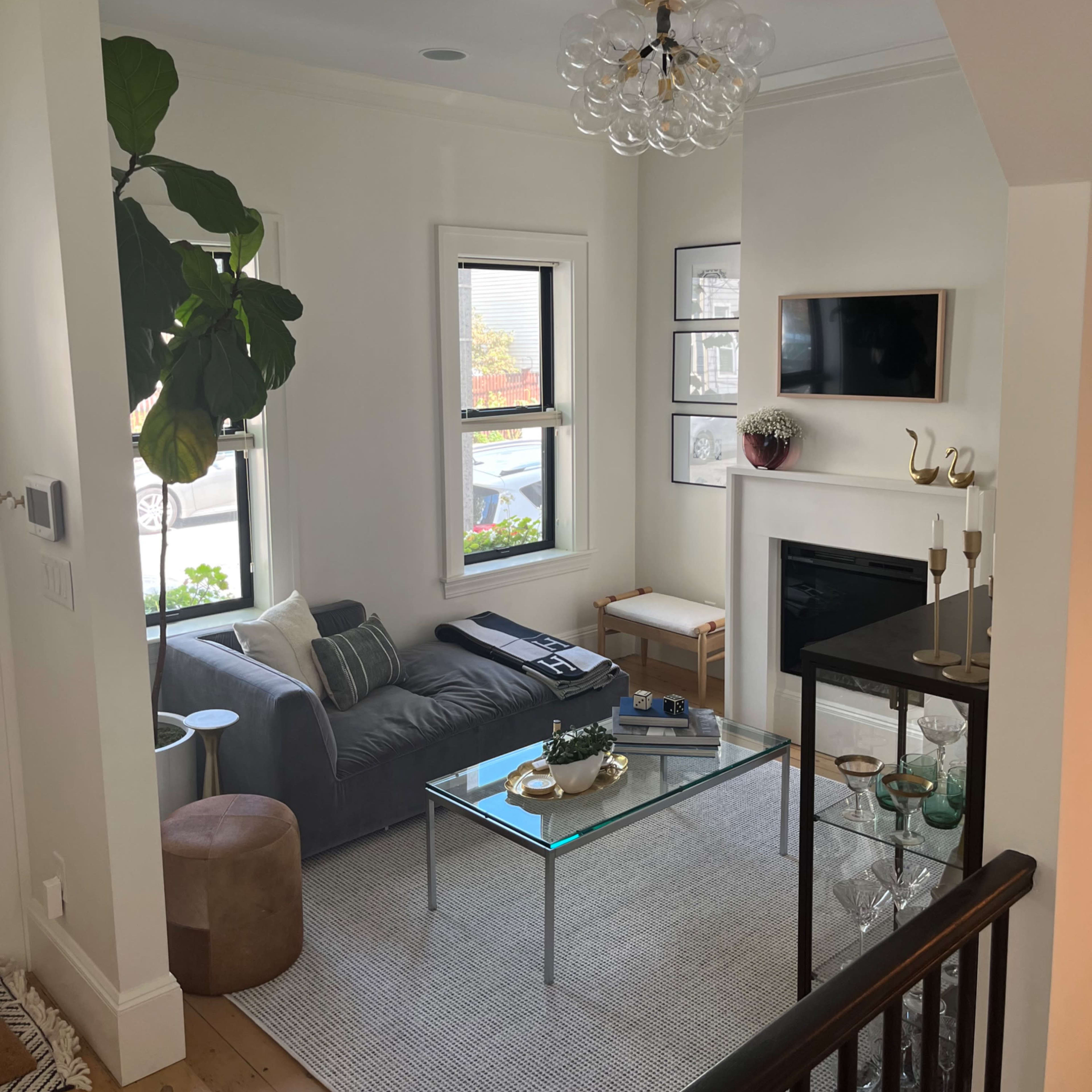 A modern living room with a gray sofa, a glass coffee table, a fireplace, and a plant in the corner.