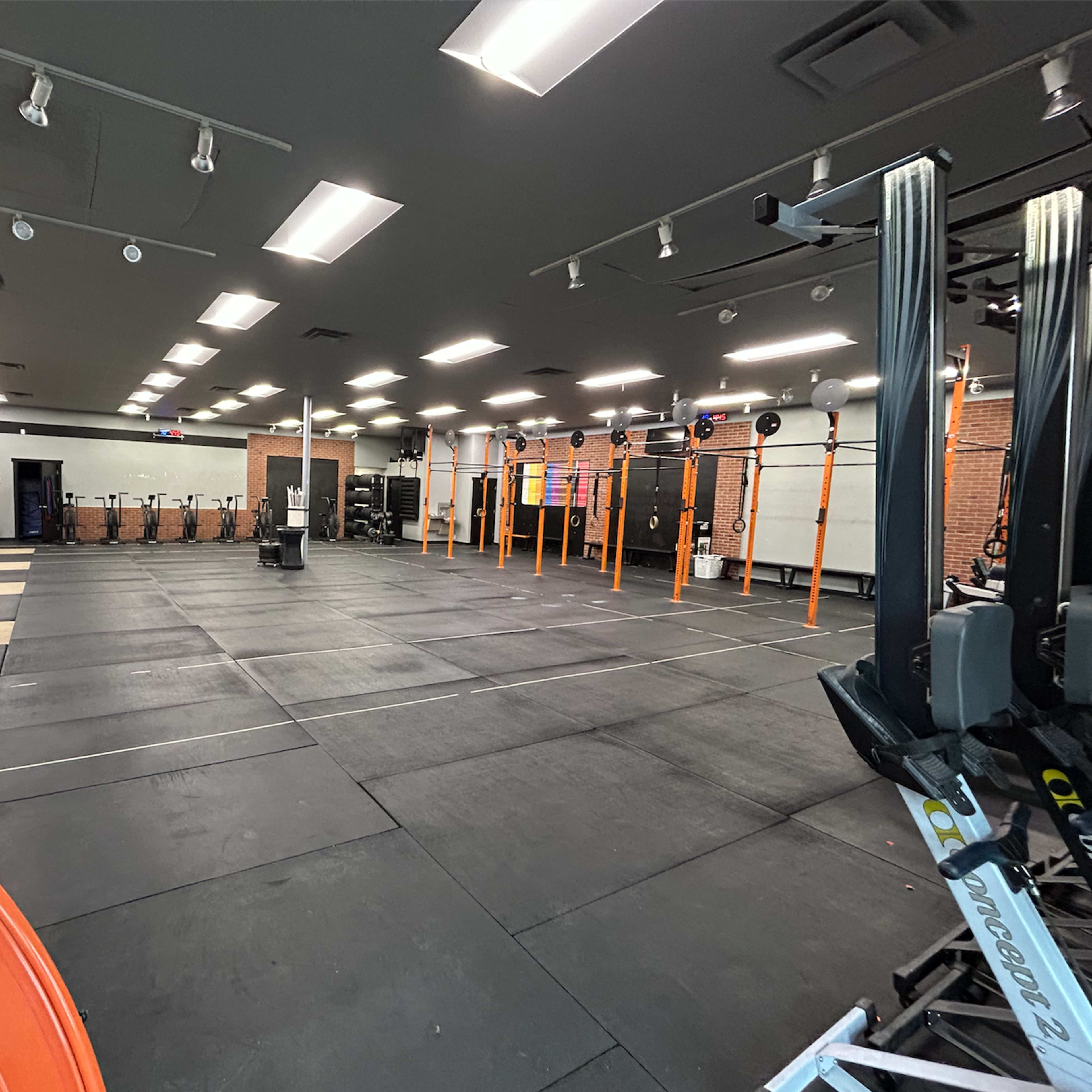 An empty gym space with weightlifting equipment, platforms, and exercise machines arranged on a black rubber floor.