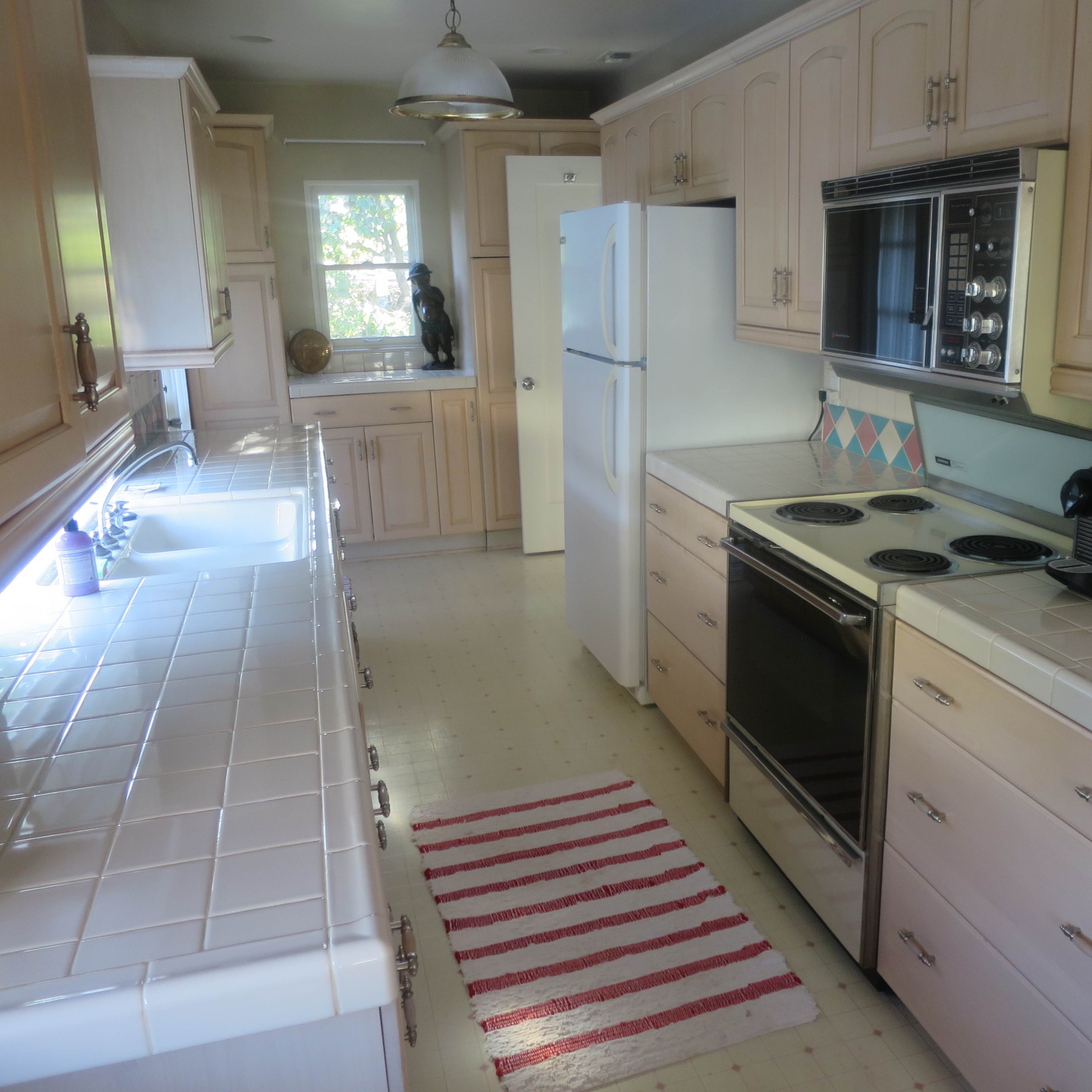 A kitchen with beige cabinetry, white countertops, and various appliances, including a refrigerator and an oven, arranged along the walls.
