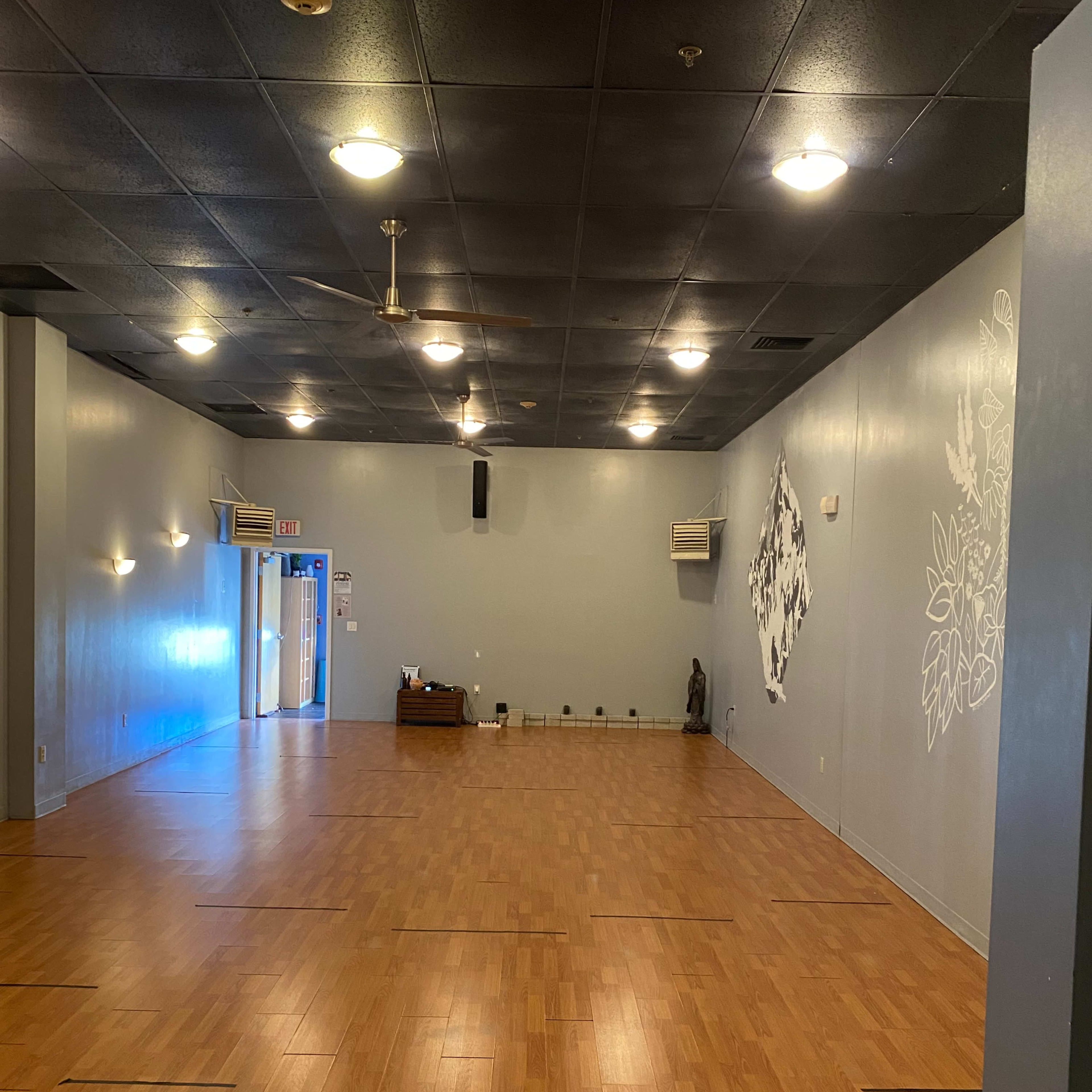 An empty room with wooden flooring, gray walls, and ceiling lights, featuring a few air conditioning units and a decorative element on one wall.