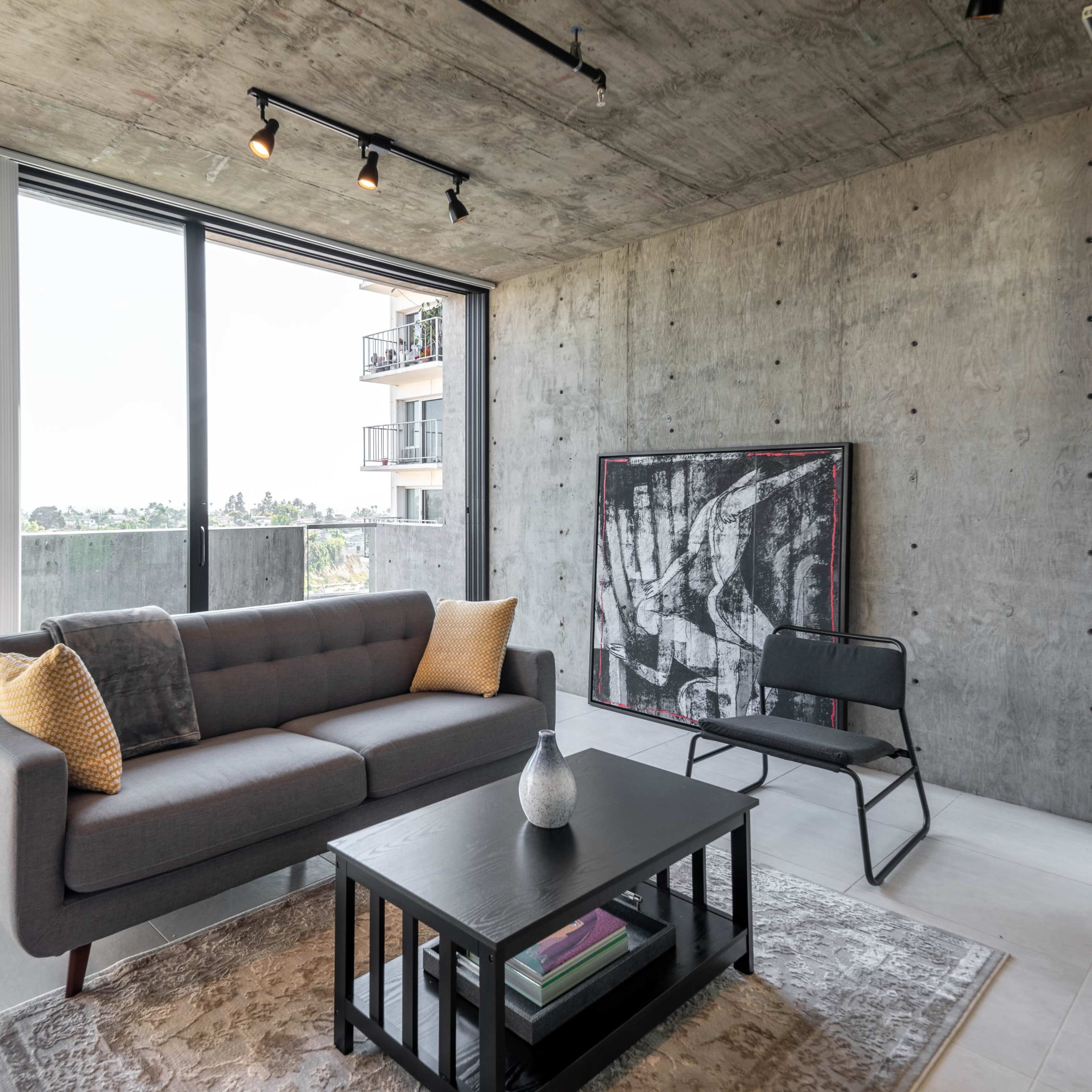 A modern living room with a gray couch, a black coffee table, and a large window displaying an outdoor view.