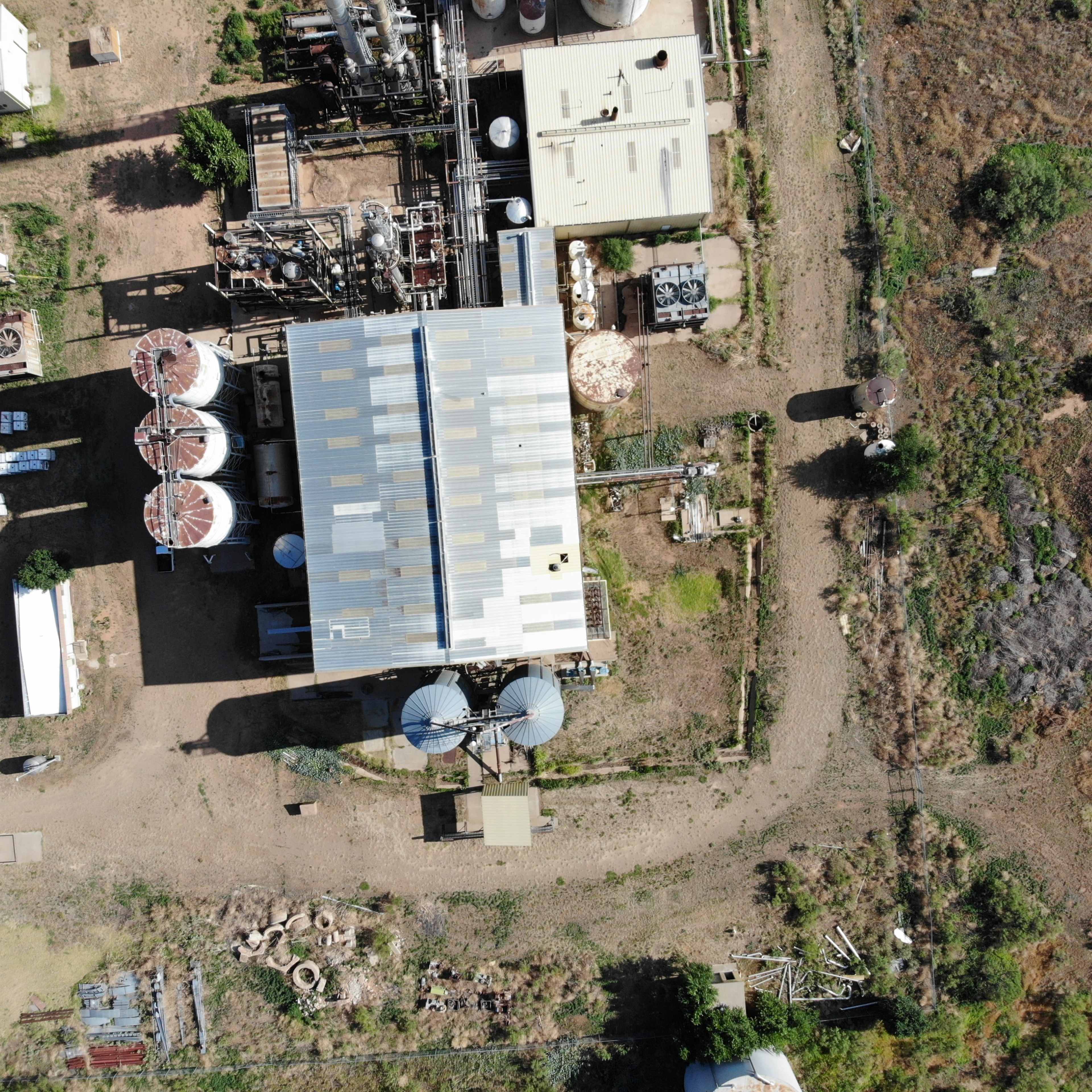 An aerial view of an industrial facility with several structures, including a large corrugated roof and multiple storage tanks.