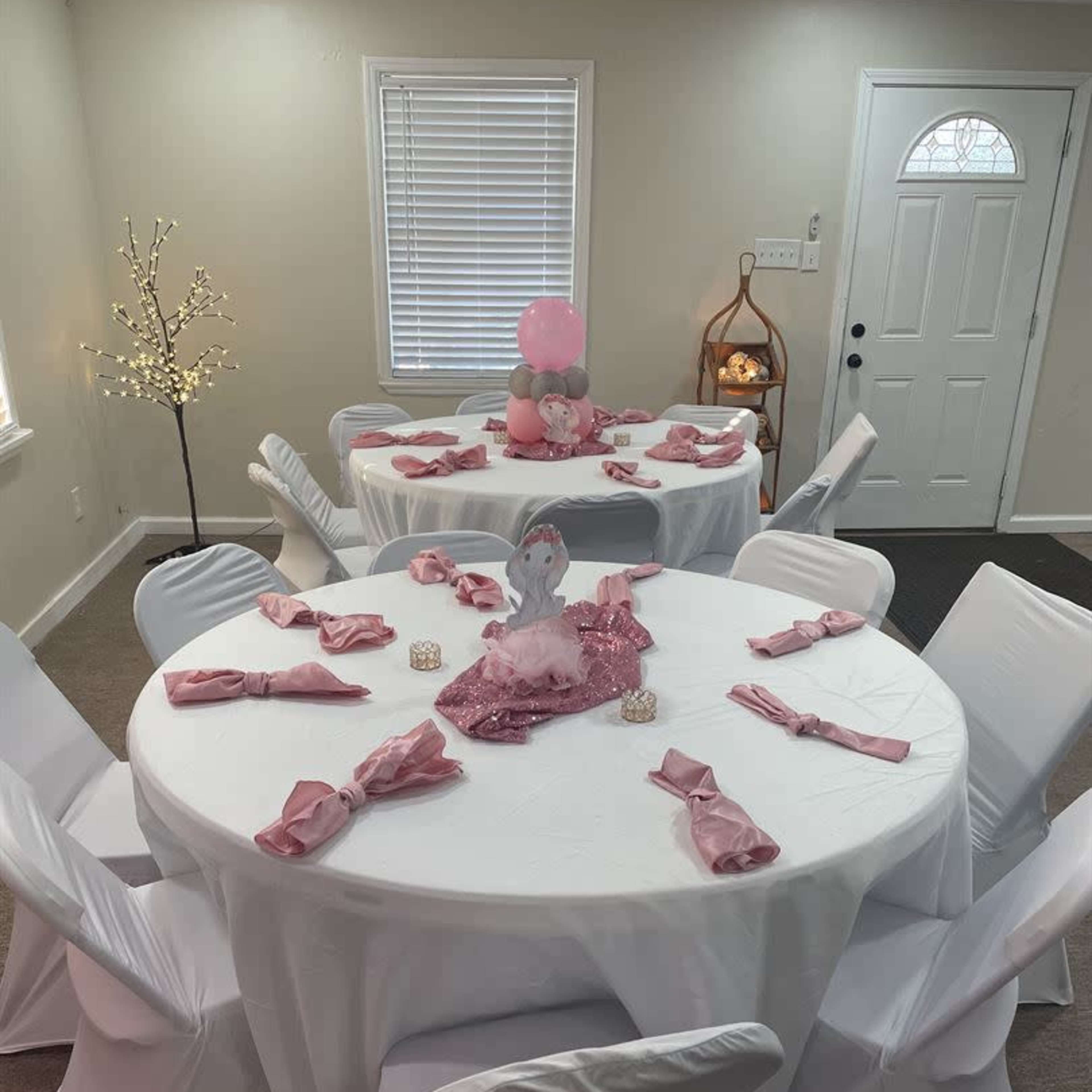 A banquet area with multiple round tables covered in white tablecloths, each set with pink napkins and a decorative centerpiece.