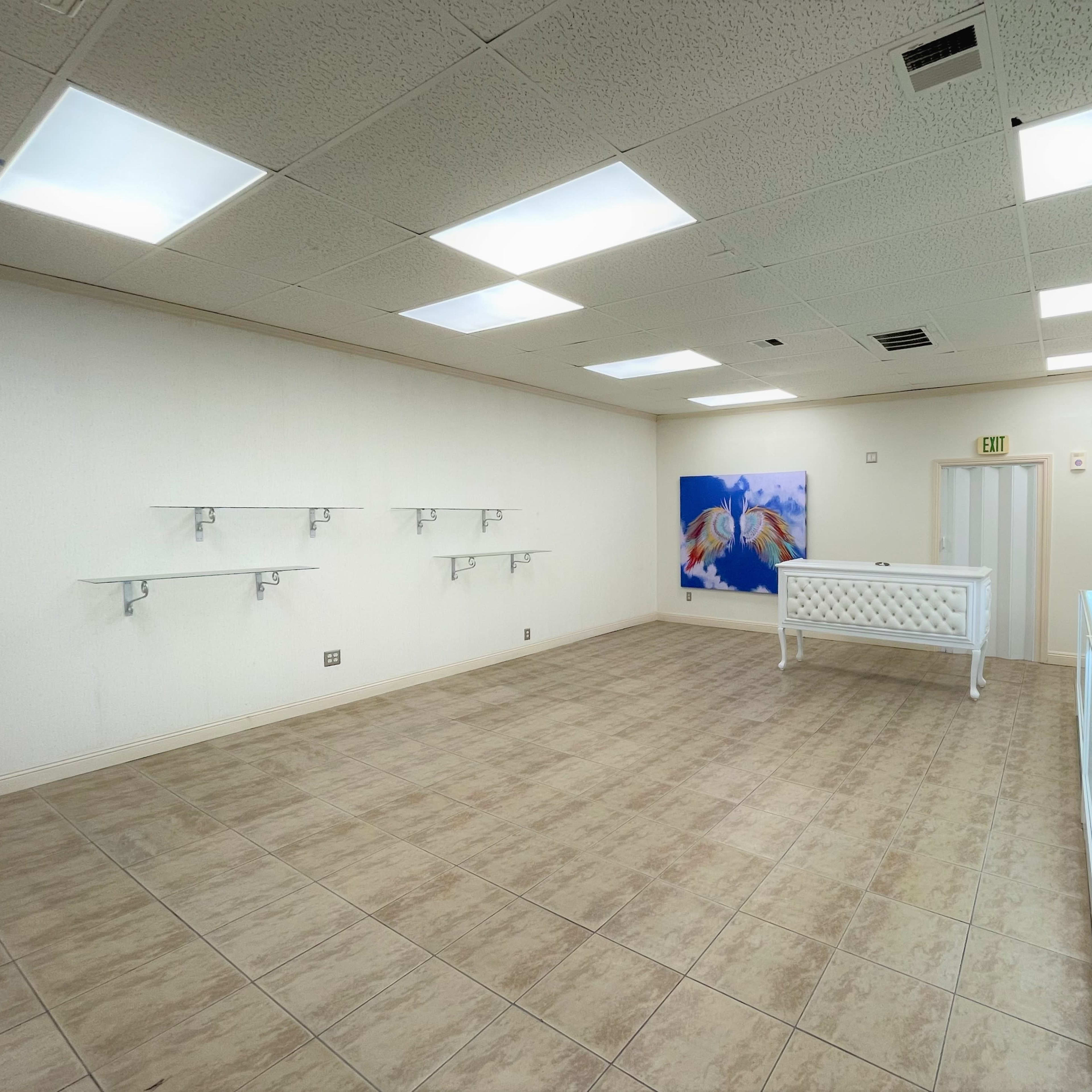 The interior of a vacant retail space features white walls, tiled flooring, a pink display case at the center, and minimal shelving on the walls.