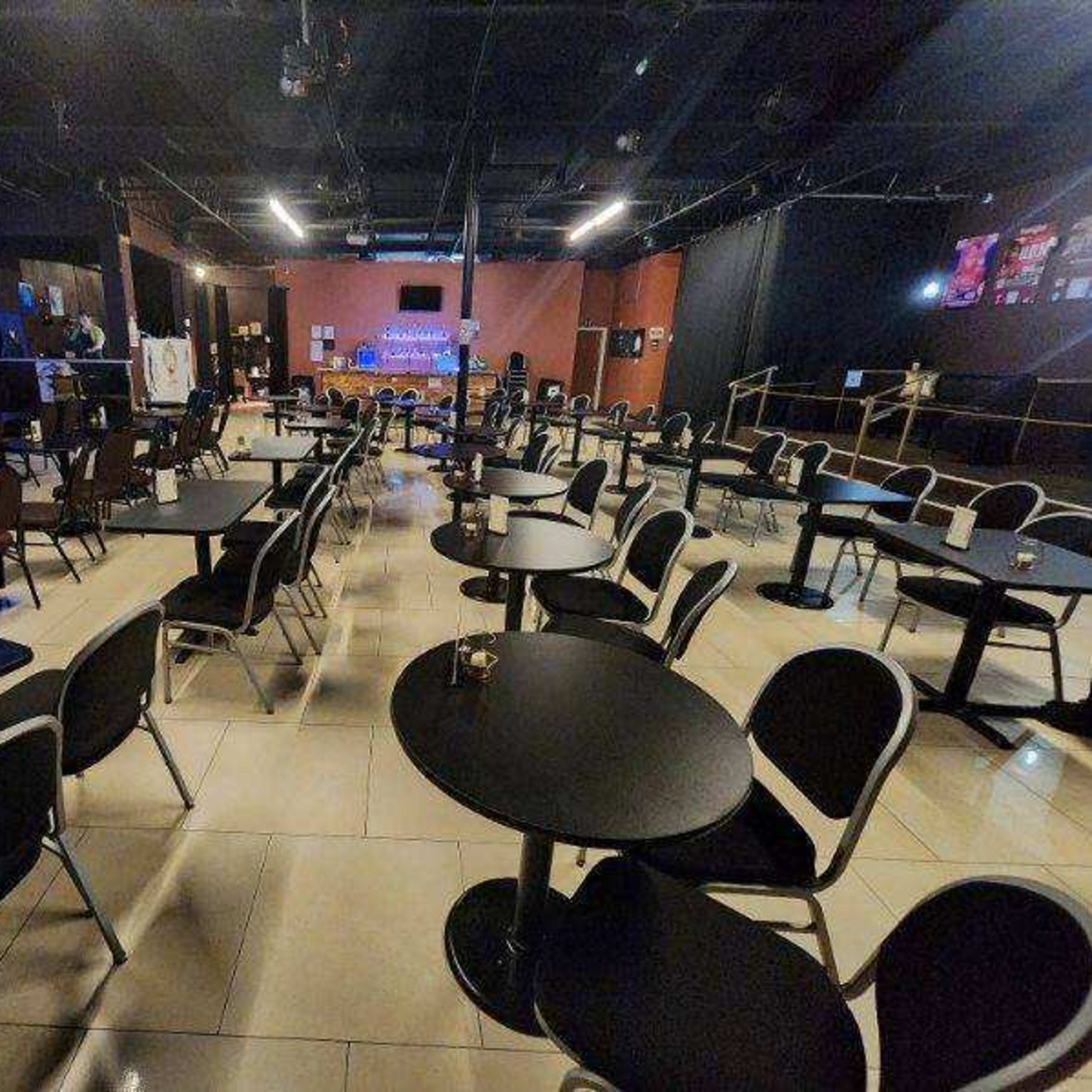 An empty indoor venue with rows of round tables and chairs arranged for an event, accompanied by a stage at the front.