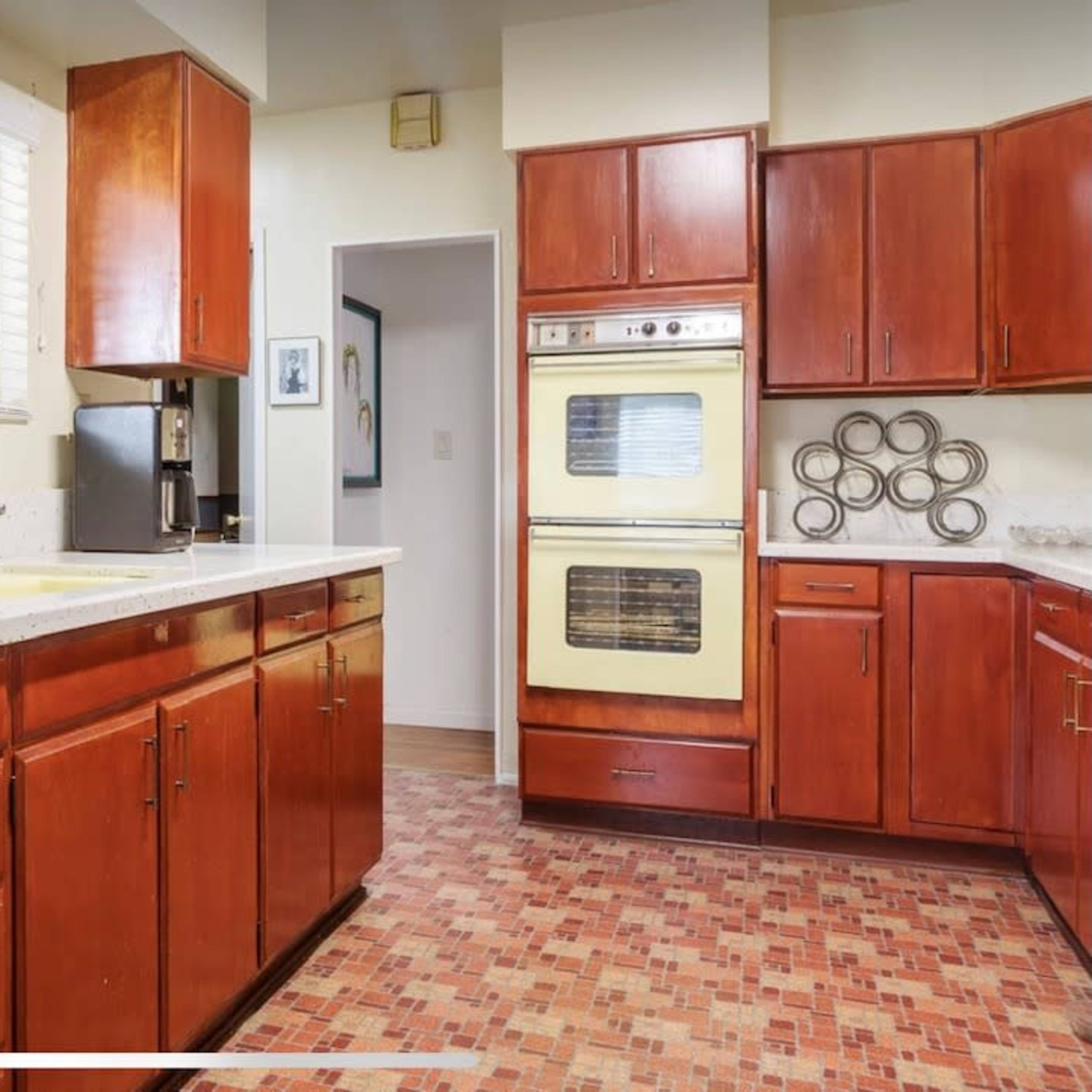 A kitchen with wooden cabinets, a stainless steel dishwasher, a yellow double oven, and a countertop beneath a window.