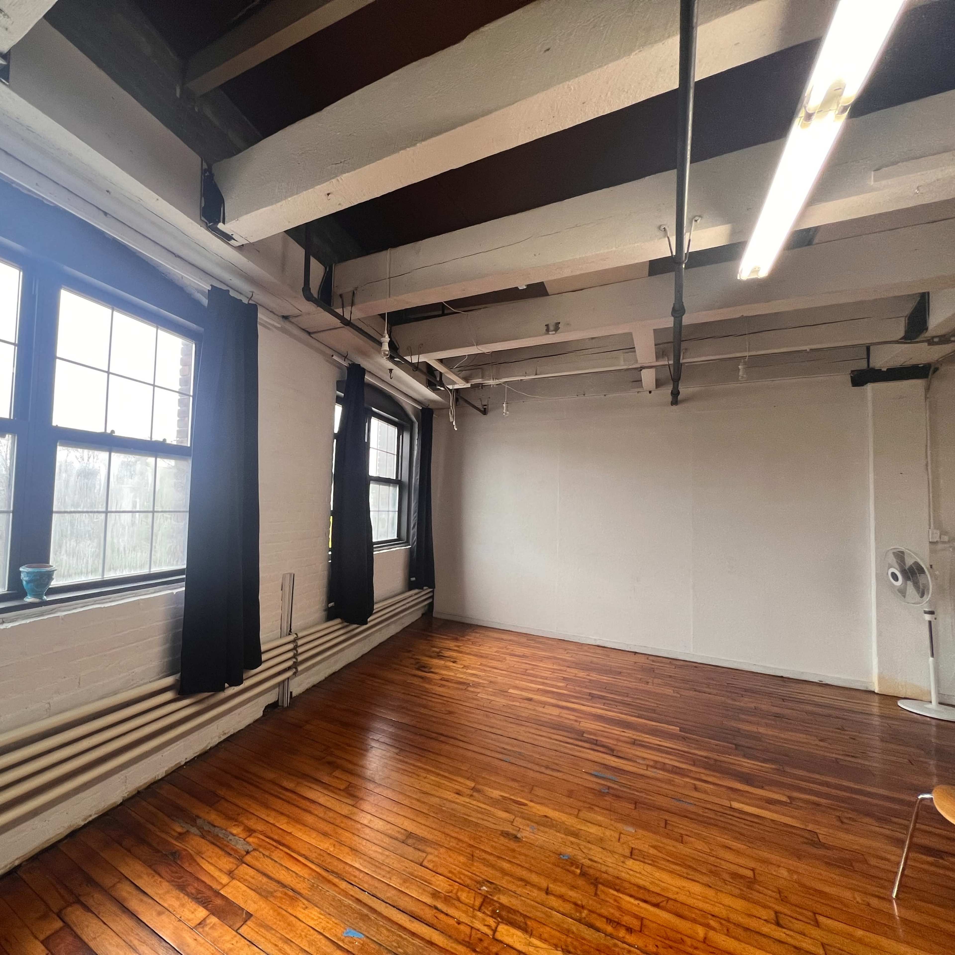 The room features large windows with black curtains, wooden flooring, and exposed beams on the ceiling.