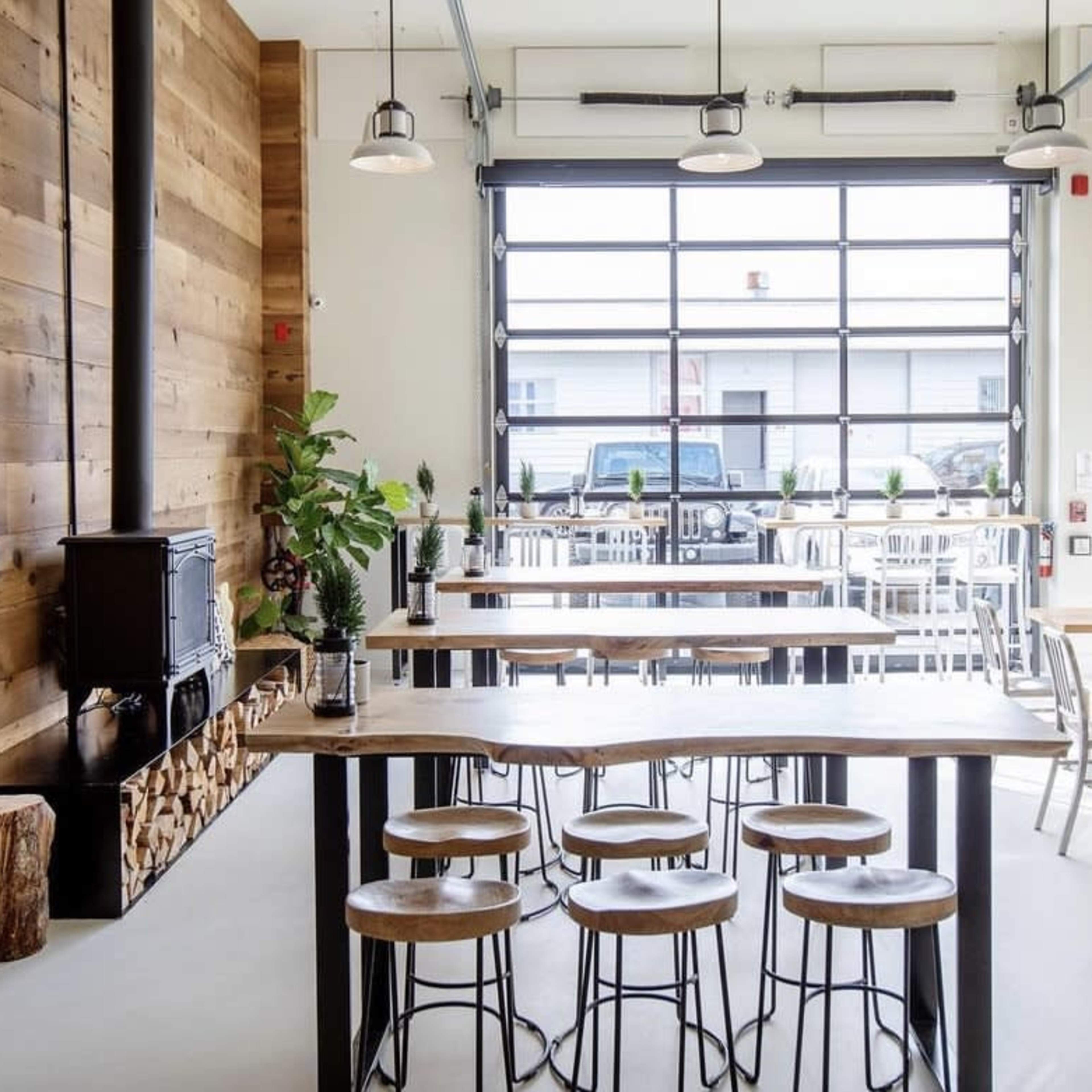 A modern café interior with wooden walls, long tables, and bar stools, featuring large windows that provide natural light.